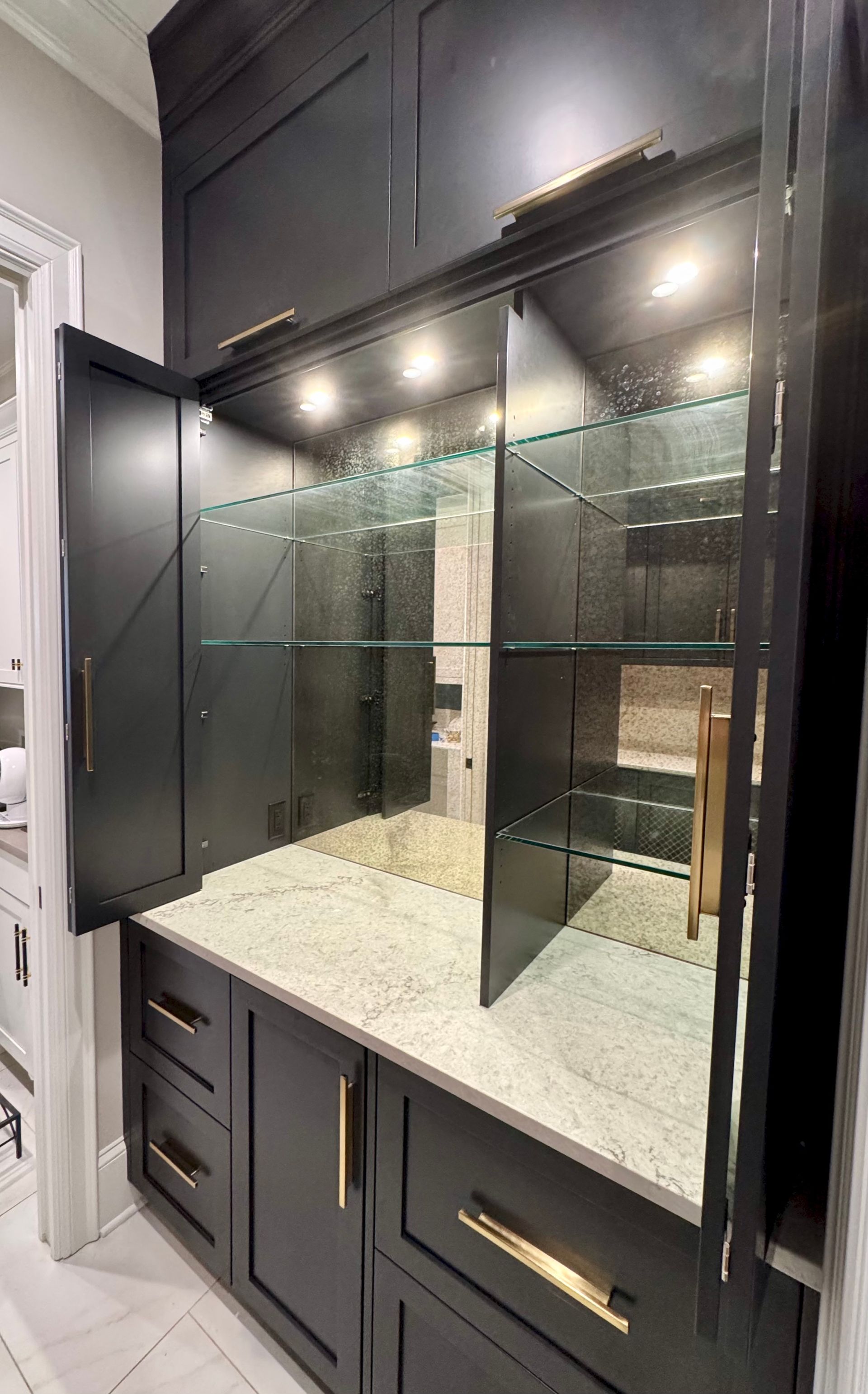A kitchen with black cabinets and a bar with glass shelves and a mirror.