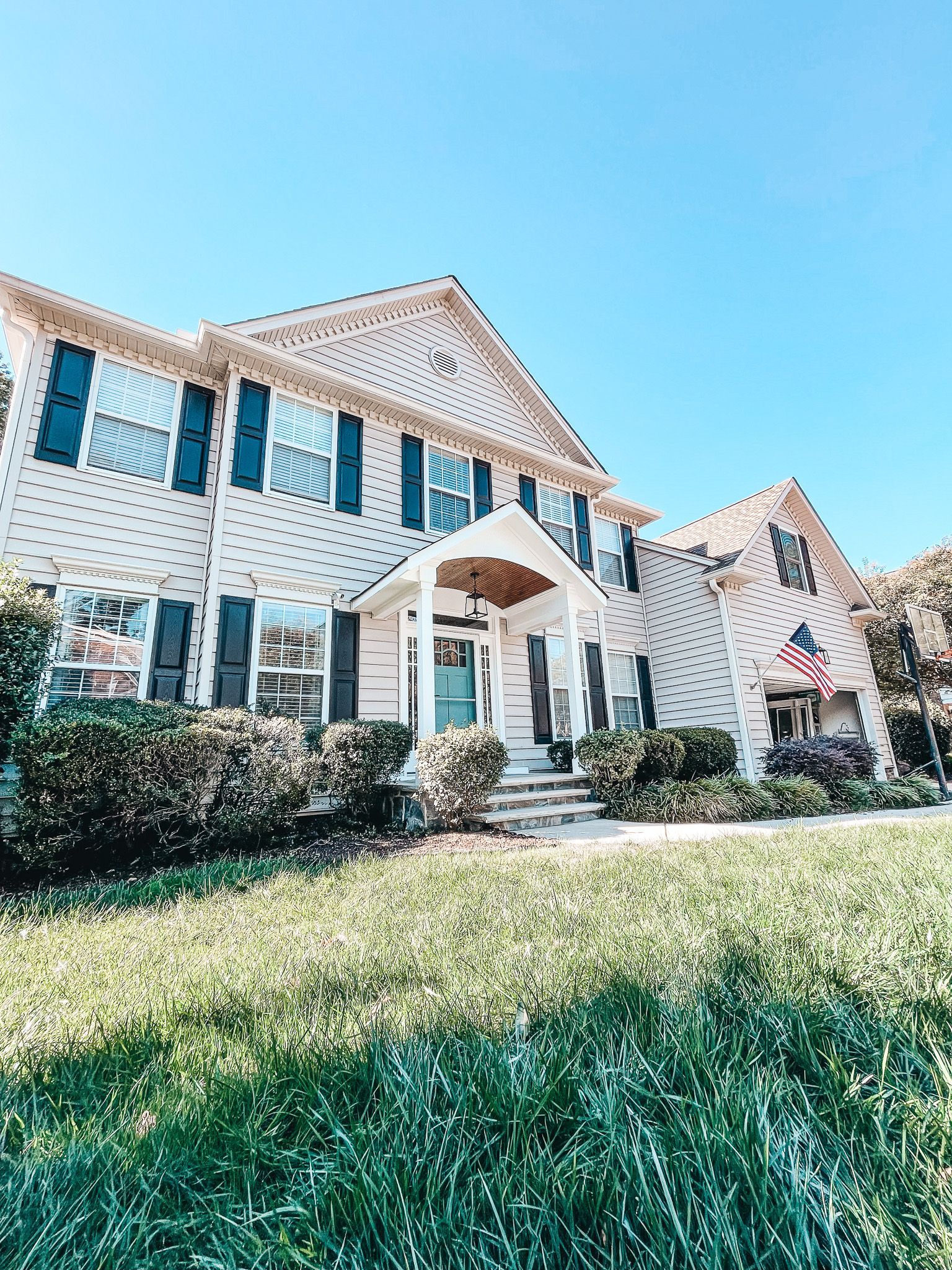 A large white house with black shutters is sitting on top of a lush green lawn.