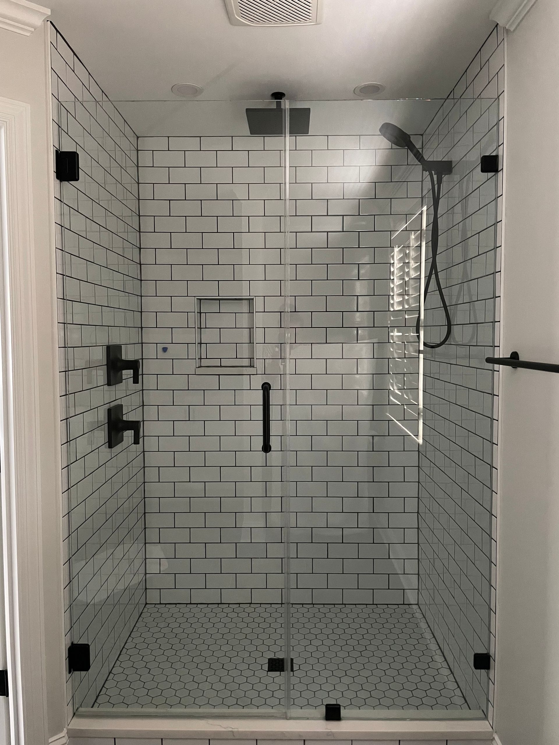 A bathroom with a walk in shower with a glass door and a shower head.