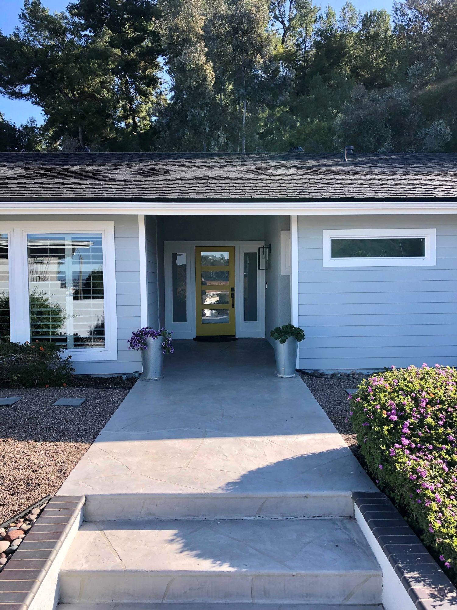 Light blue house with yellow front door, concrete path, and two silver planters.