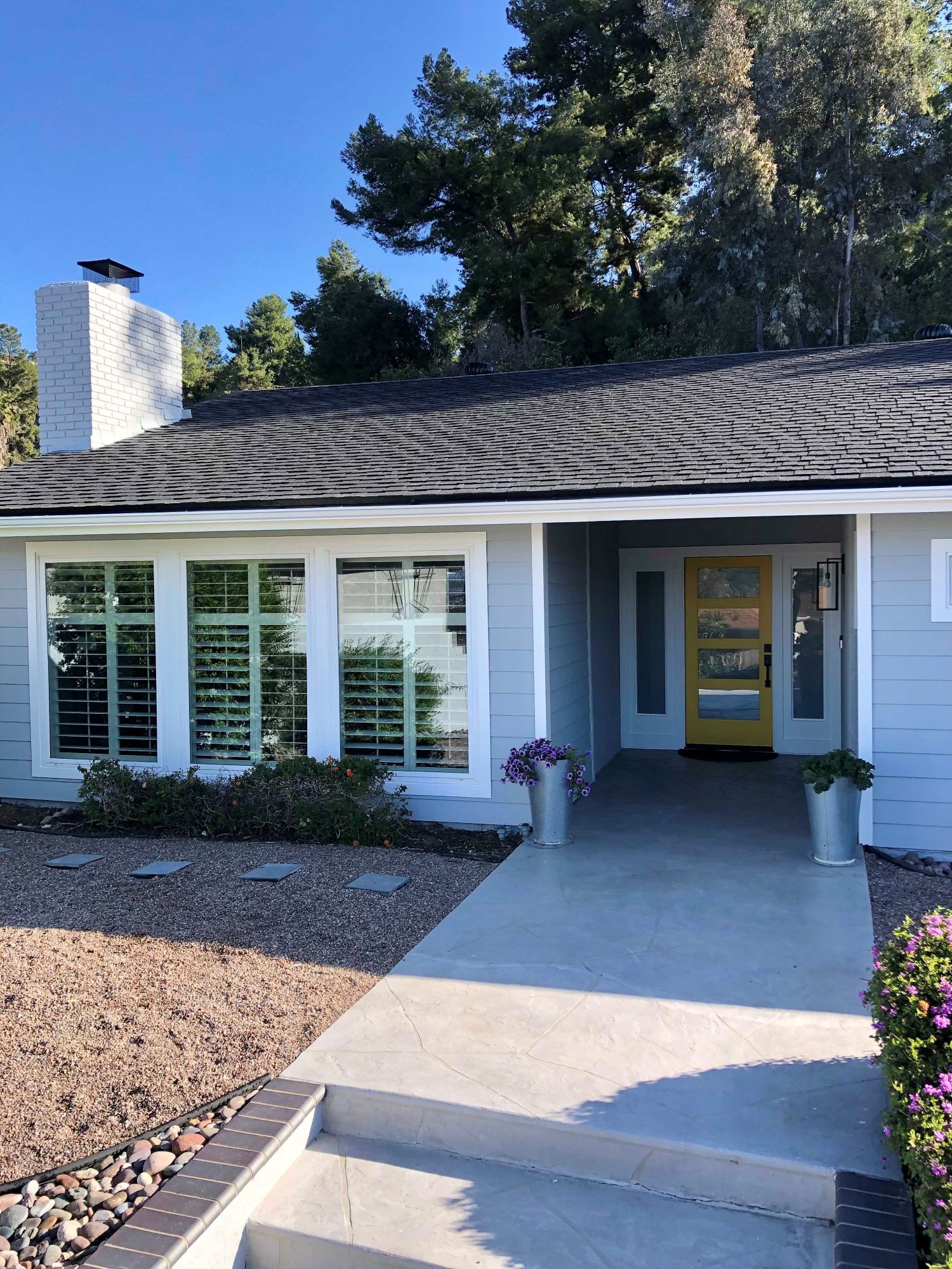 Light blue house with a yellow door, white shutters, and a concrete path.