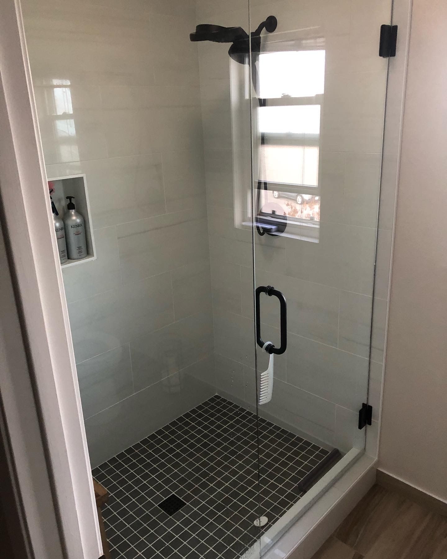 Modern shower with glass door, black fixtures, and gray tile floor and walls.