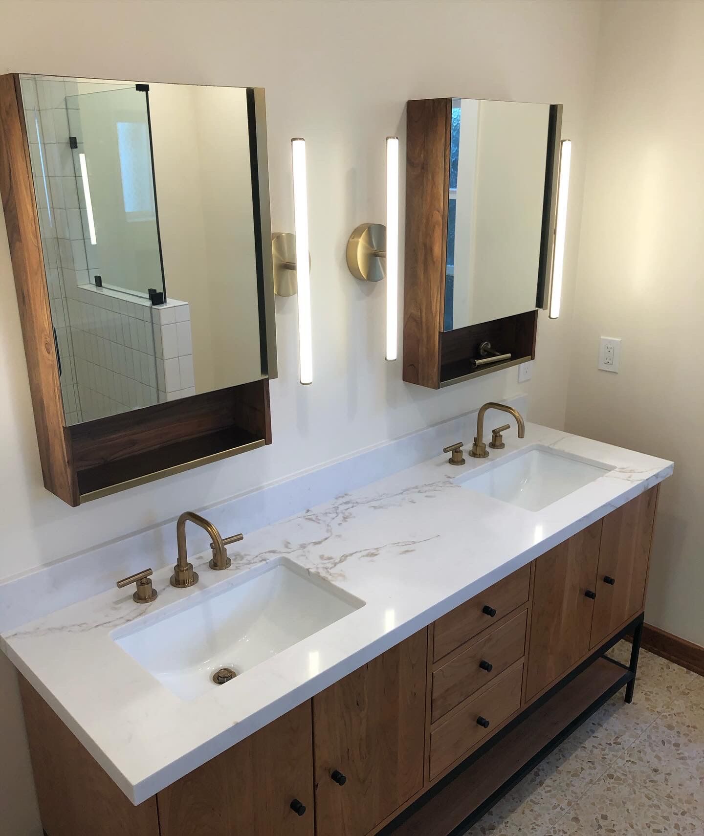 Bathroom vanity with two sinks, wood cabinets, mirrors, and gold fixtures.