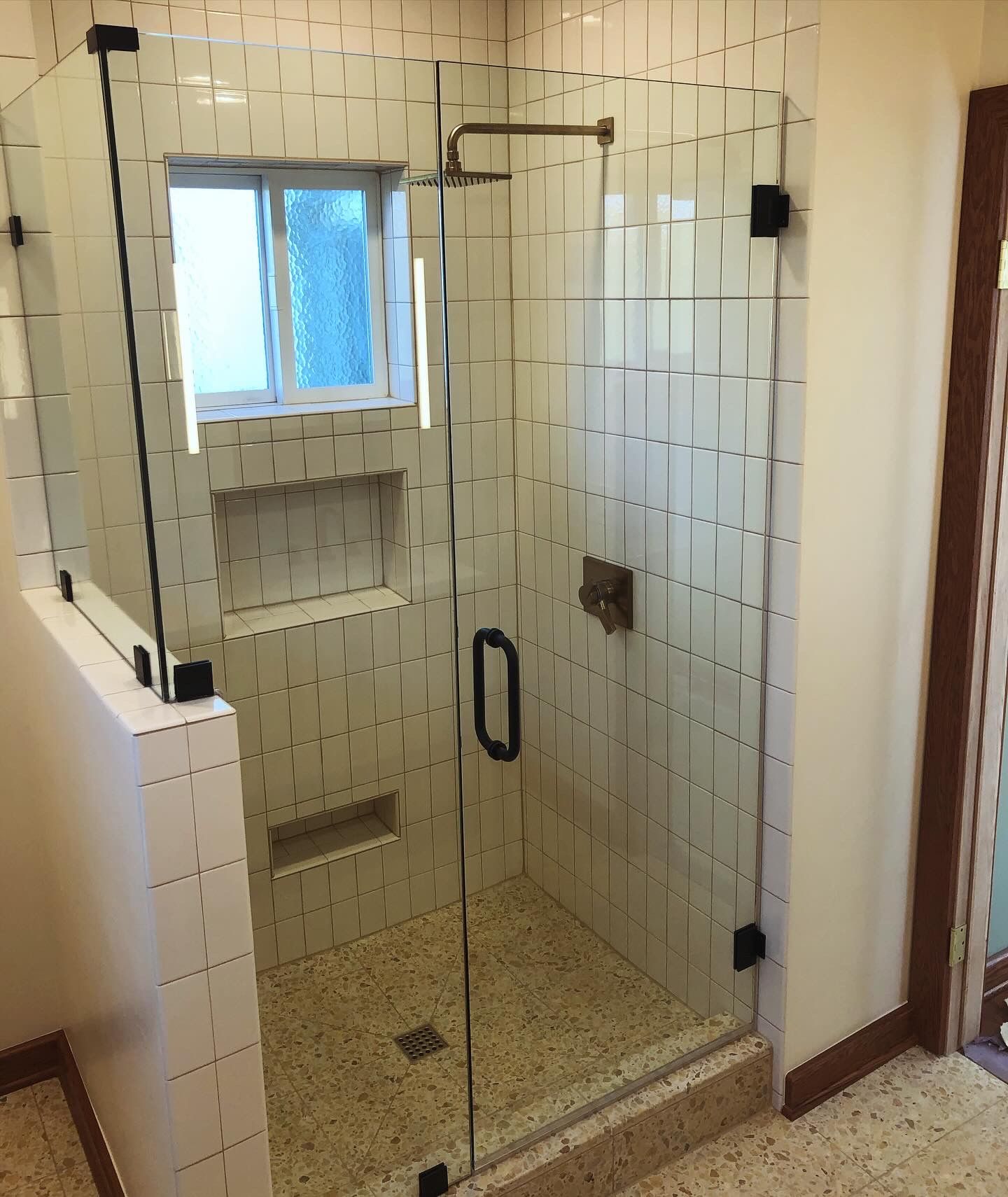 Glass shower enclosure with white tile walls, a small window, and a pebble floor.
