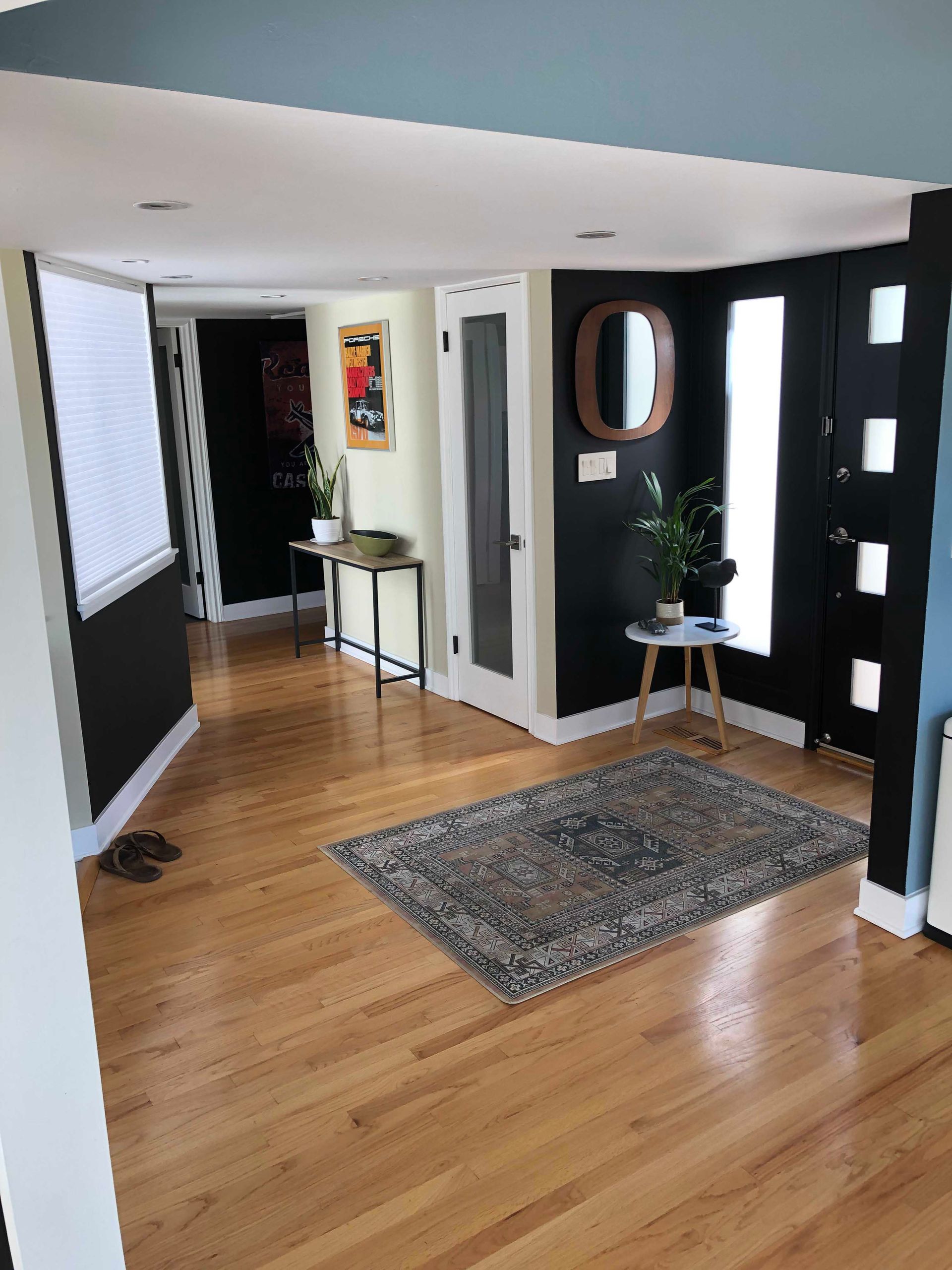 Entryway with hardwood floors, dark walls, rug, mirror, plants, and a black front door.