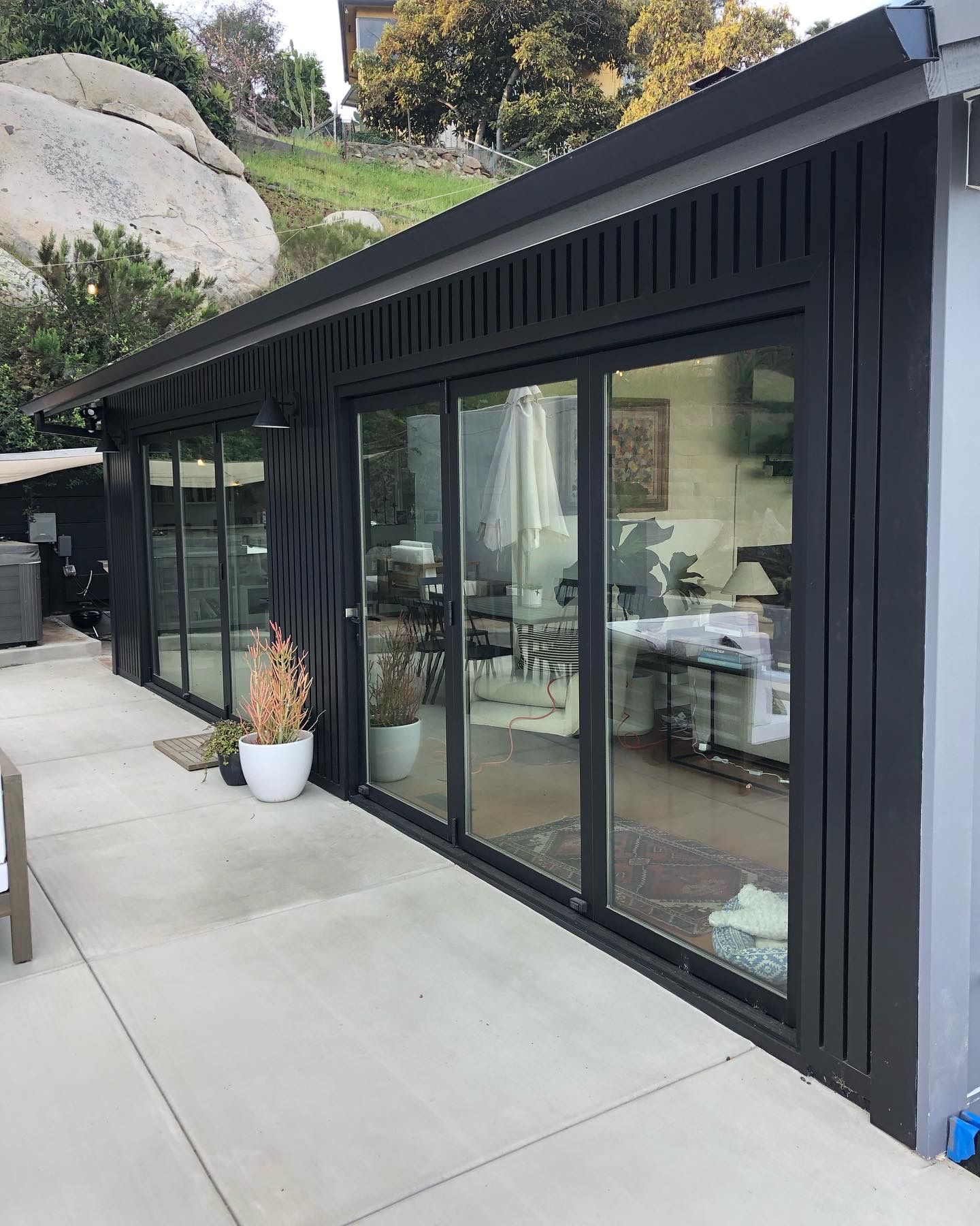 Black-framed glass doors and windows of a modern building, on a concrete patio with a view of a hillside.