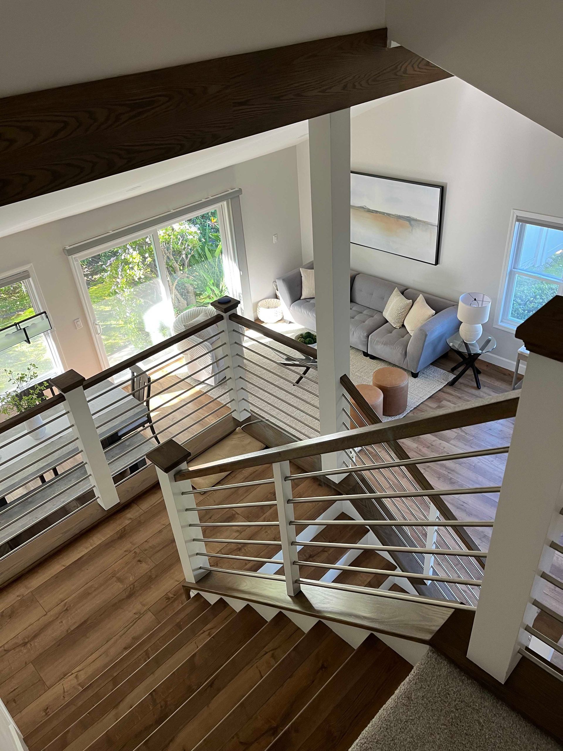 Wooden staircase leads to a living room with gray couch, large windows, and modern metal railing.