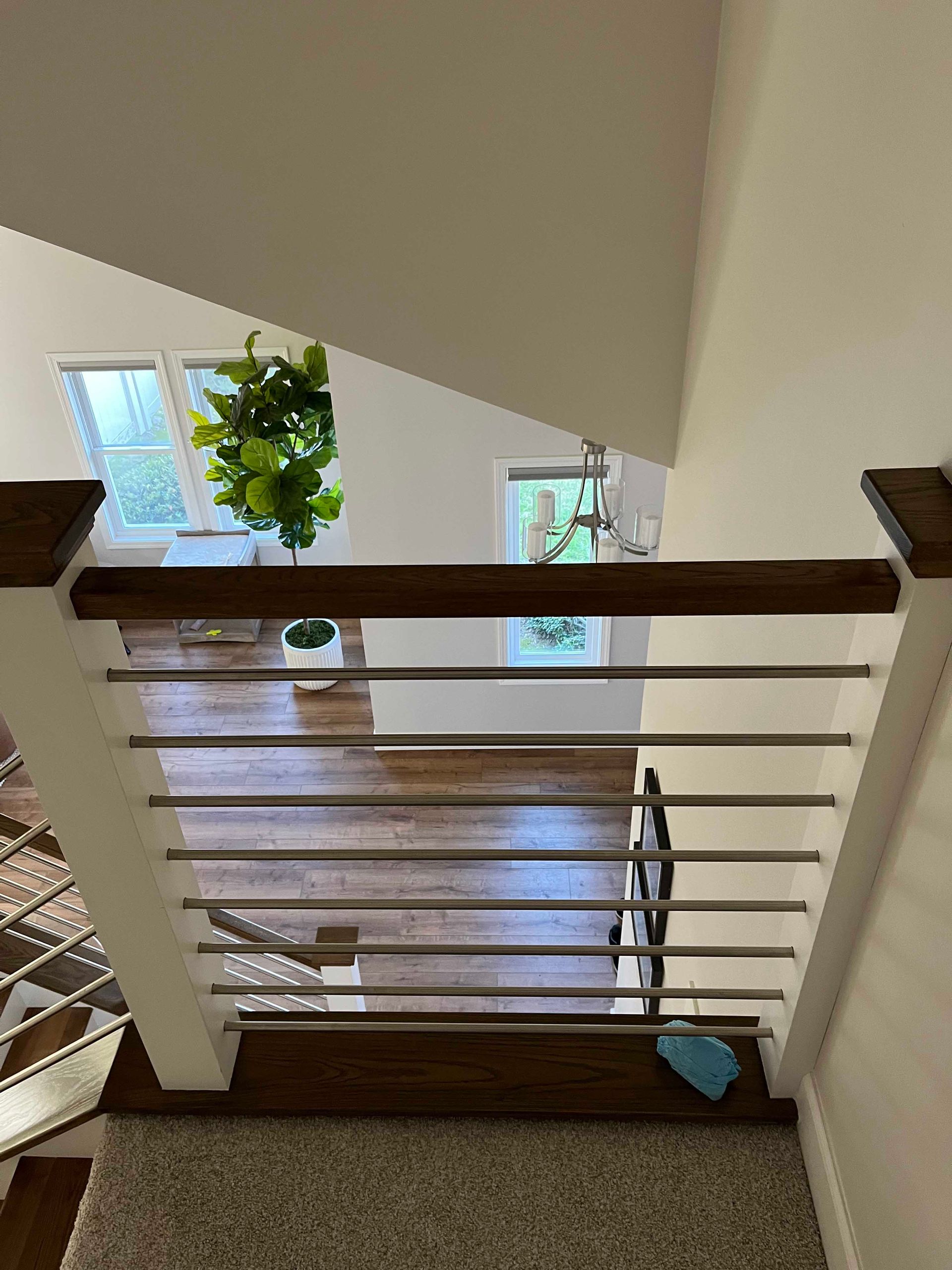 View from top of stairs. Brown railing with metal bars, hardwood floor visible. Bright natural light.