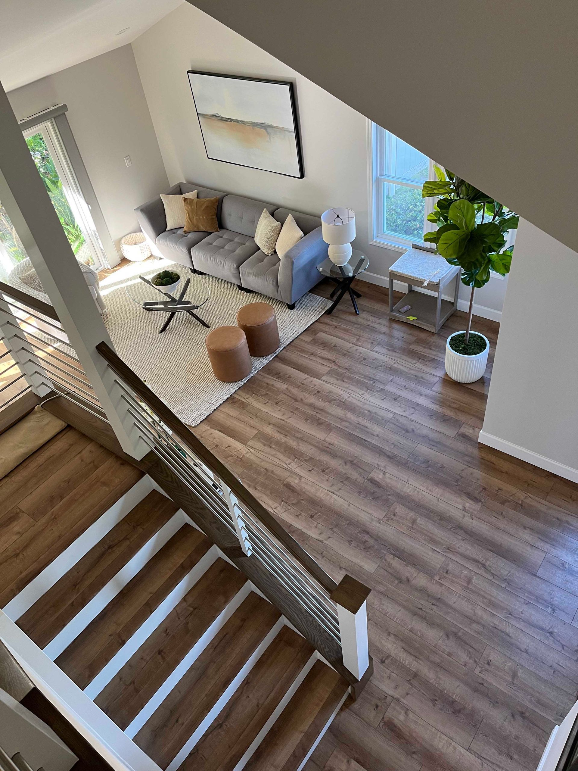Overhead view of a living room with stairs, couch, rug, and large plant. Neutral tones with natural light.