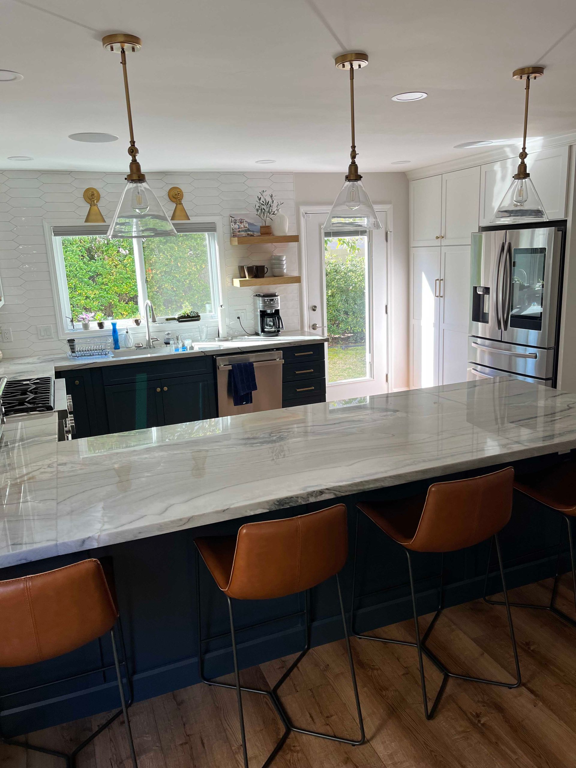 Kitchen with dark blue cabinets, light countertop, and pendant lights. Brown leather barstools.