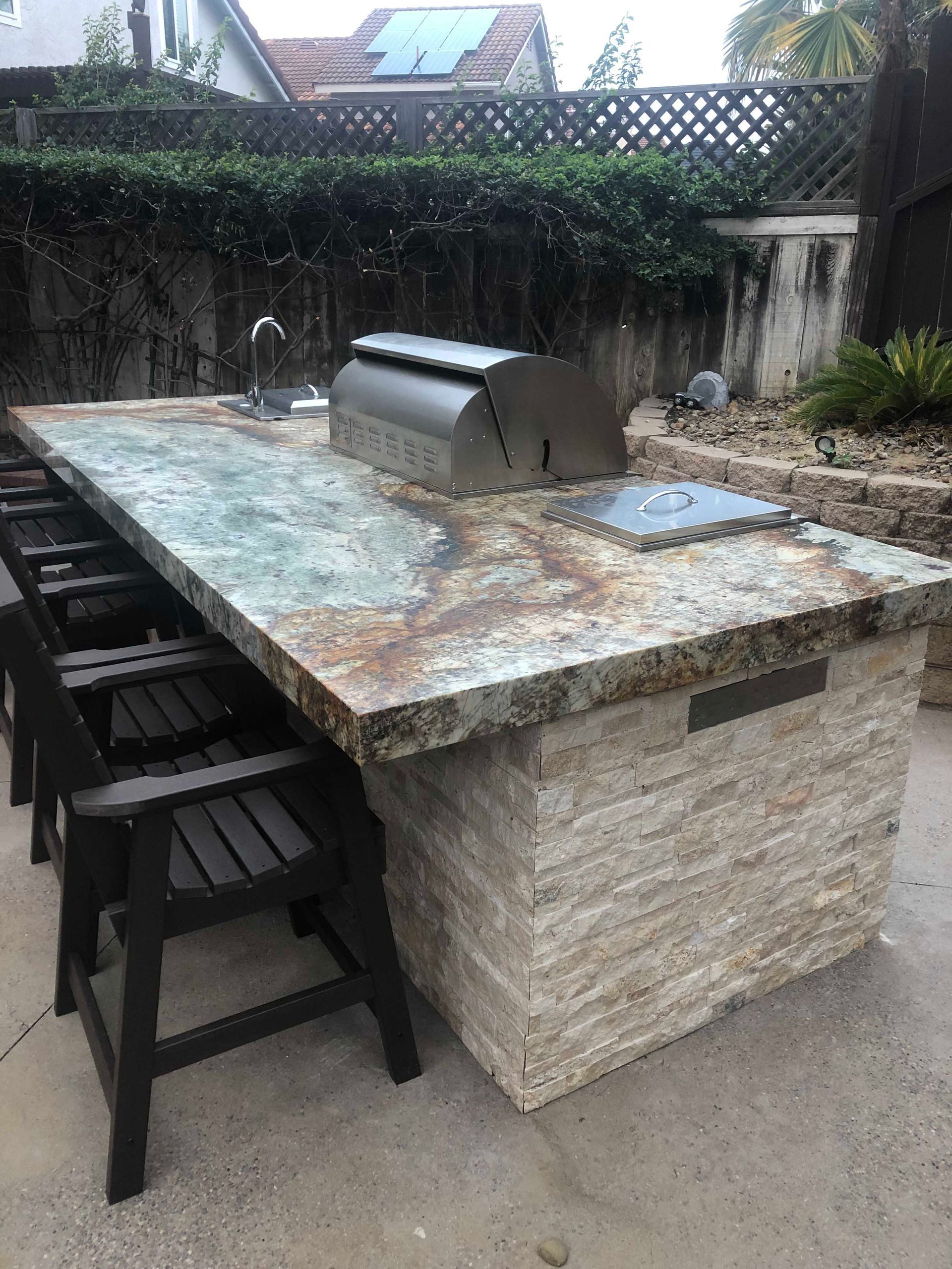Outdoor kitchen island with a granite countertop, grill, sink, and bar seating.