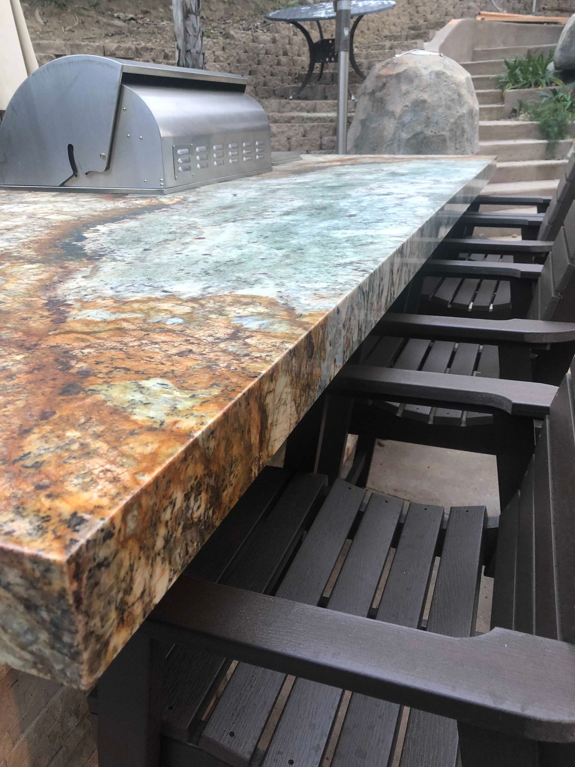 Outdoor bar with granite countertop, built-in grill, and wooden chairs.