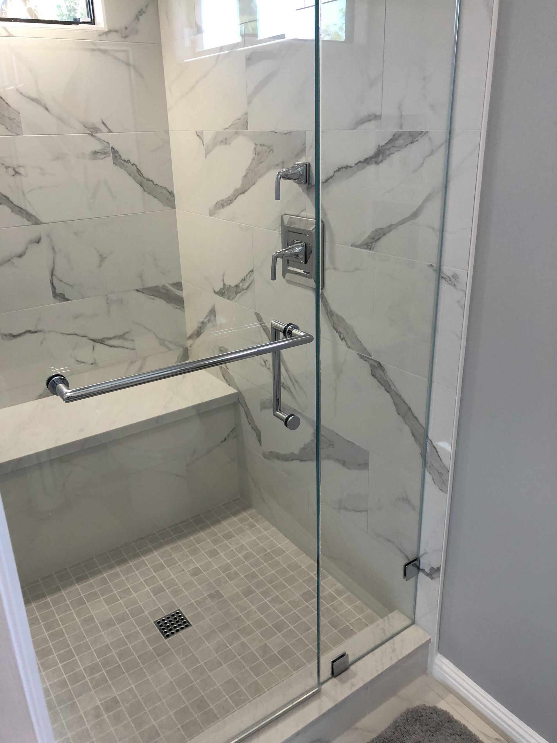 Glass shower enclosure with gray tile, marble-look wall tile, and chrome fixtures.