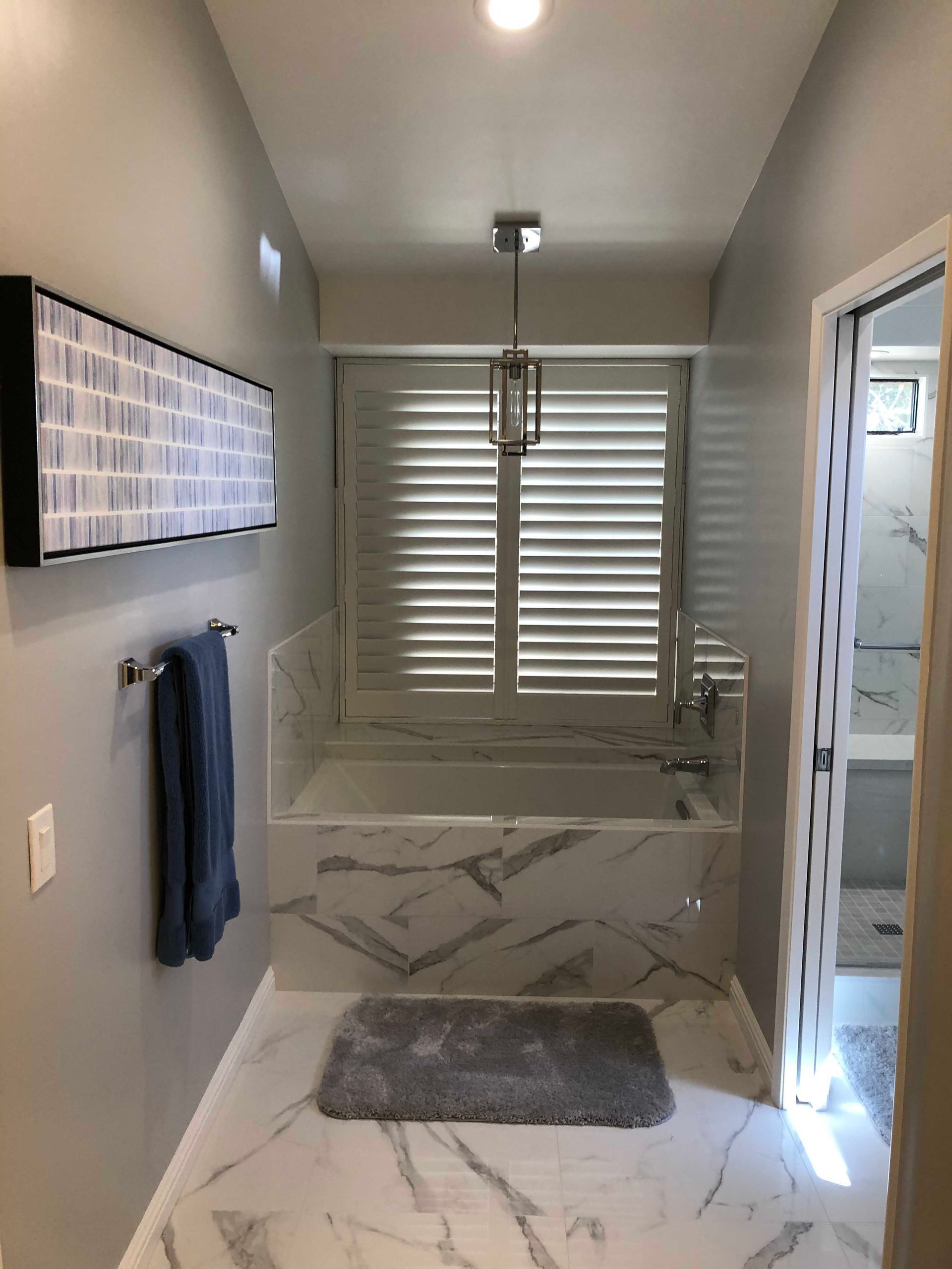 Bathroom with marble-like tile, white shutters over a tub, and a hanging light.