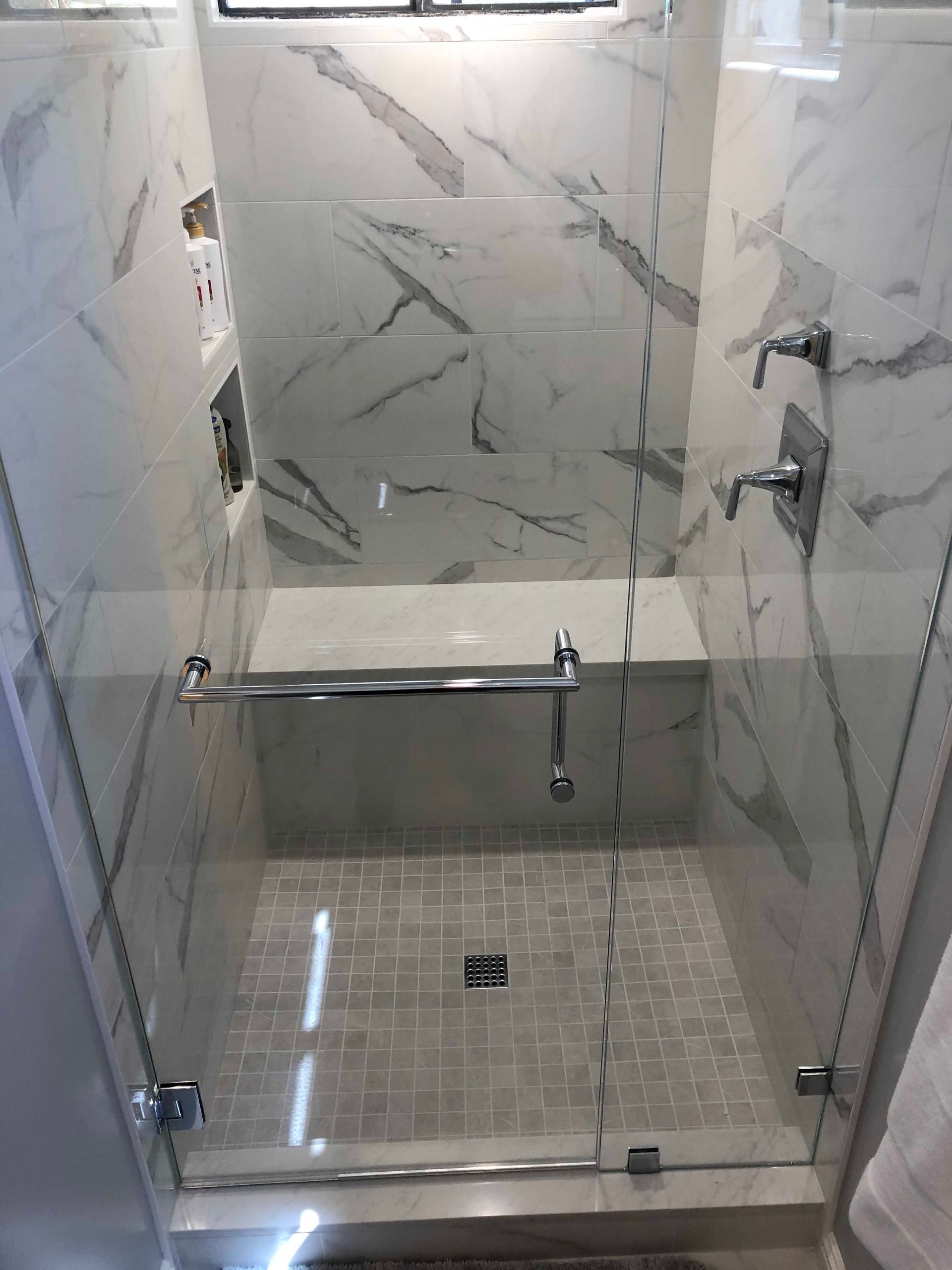 A marble-tiled walk-in shower with glass doors, a built-in bench, and silver fixtures.