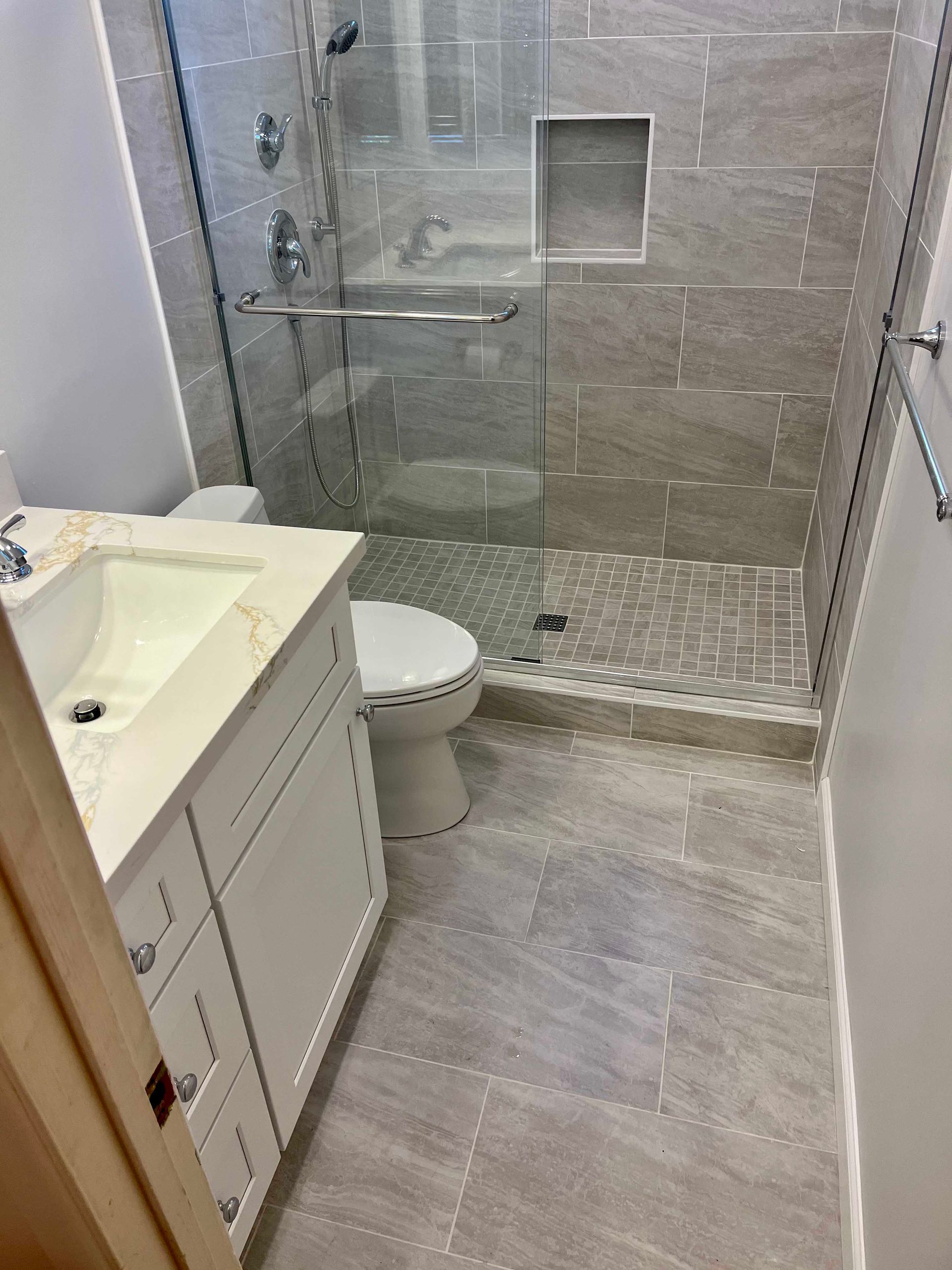 Modern bathroom with tiled shower, vanity, toilet, and gray flooring.