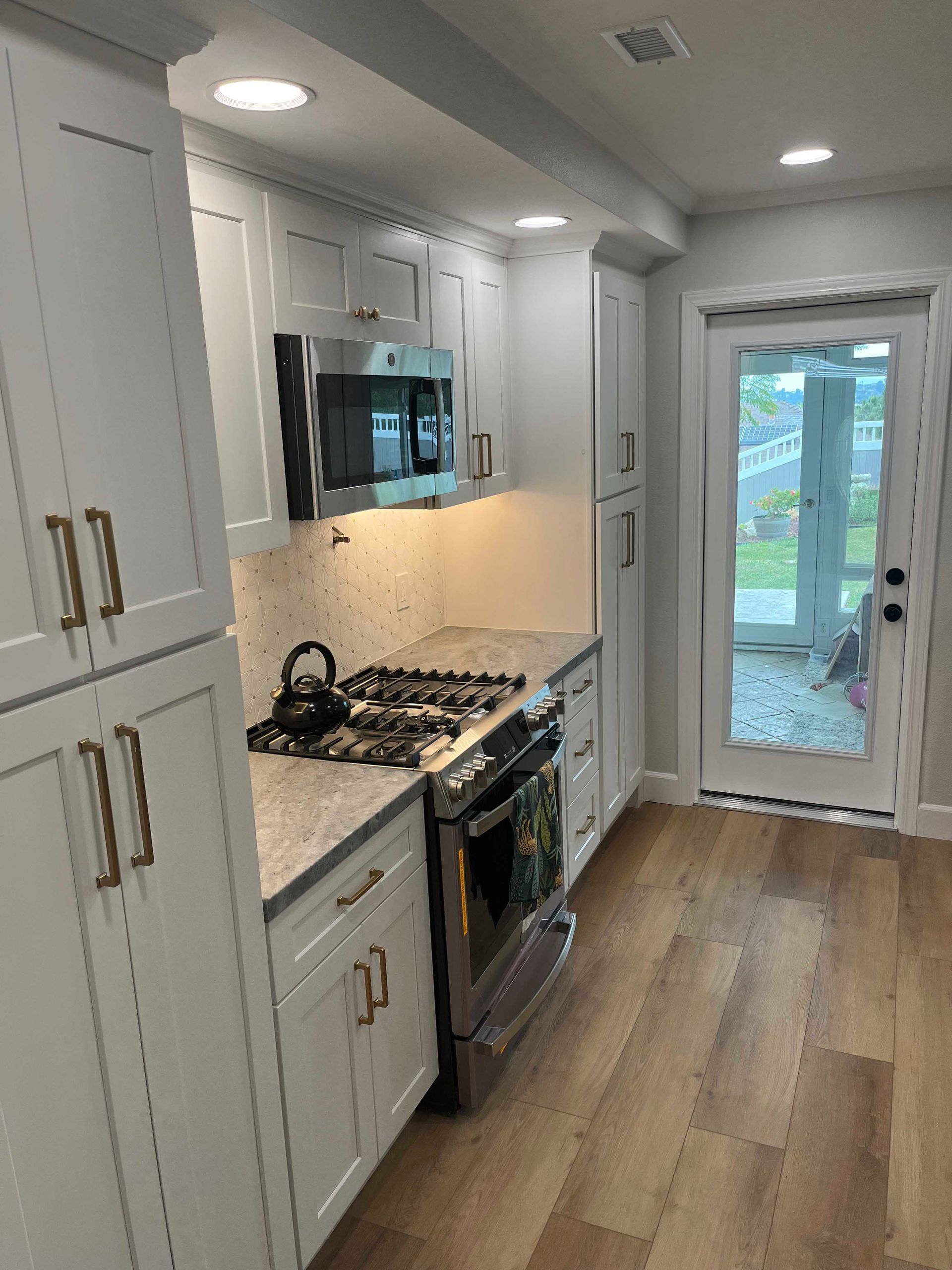White kitchen with stainless steel appliances, light countertops, and wood-look flooring. Door to outside.