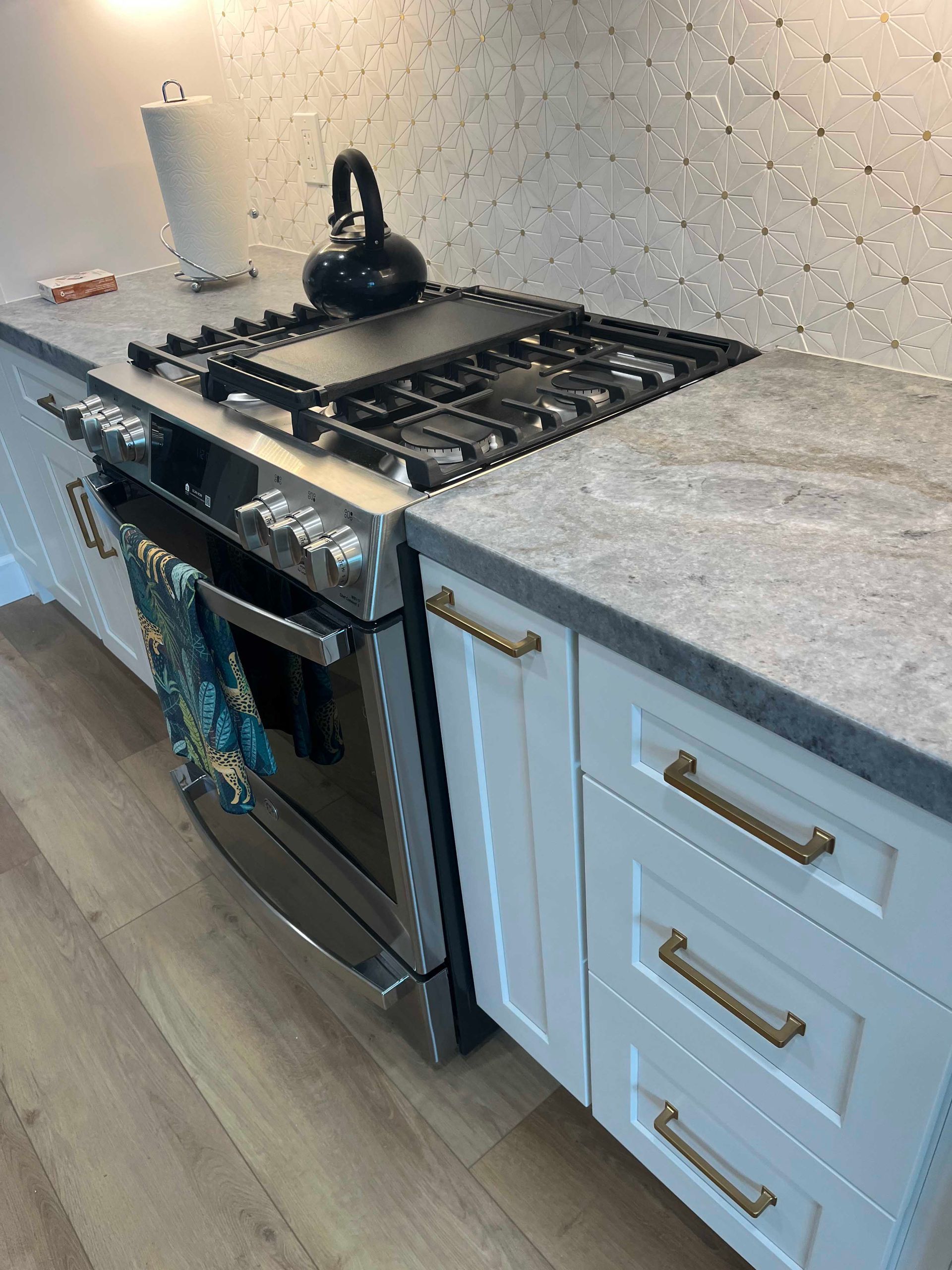 Stainless steel range in a white kitchen with gray countertops and a mosaic backsplash.