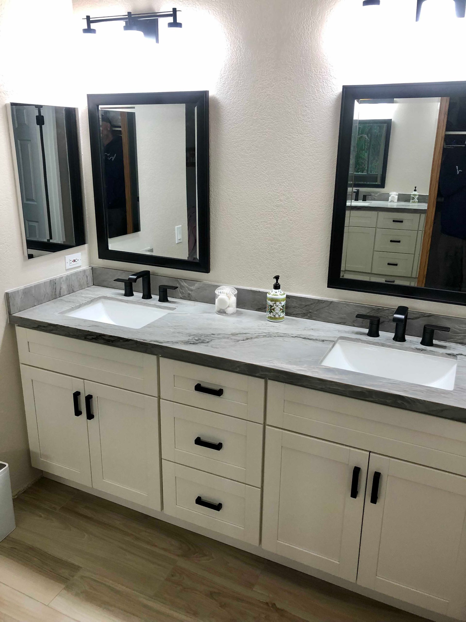 Bathroom with white cabinets, gray countertop, black framed mirrors, and black fixtures.