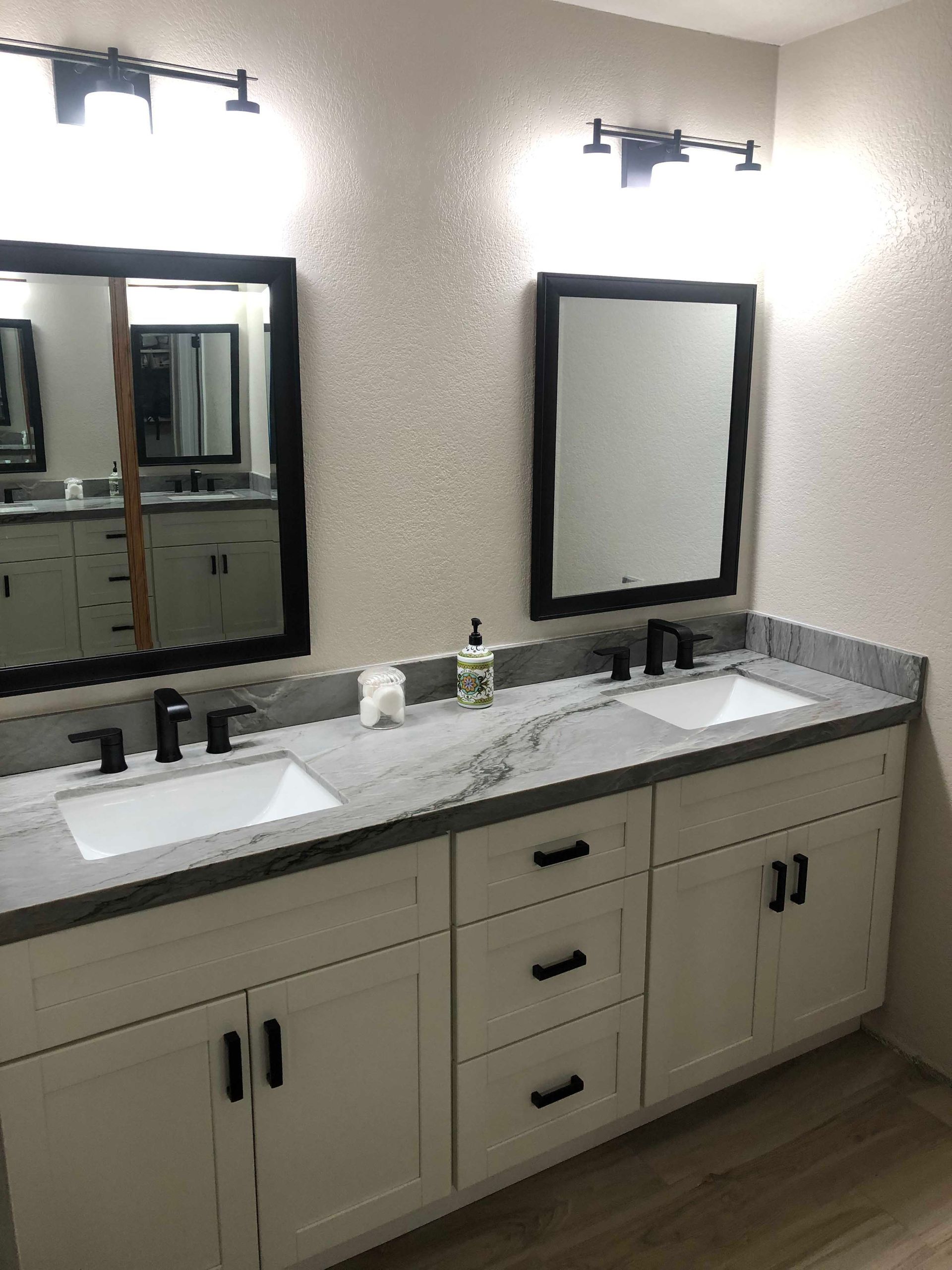Bathroom with white cabinets, gray countertop, black hardware, and two mirrors.