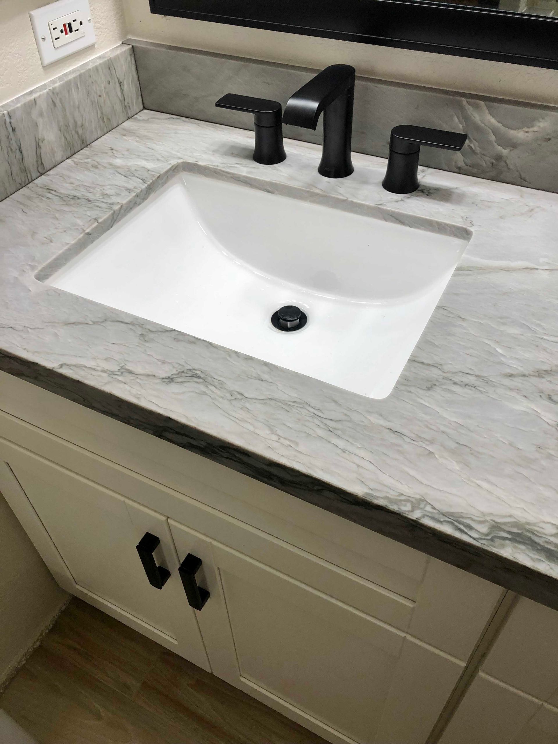 White bathroom vanity with marble countertop, black faucet, and white sink.