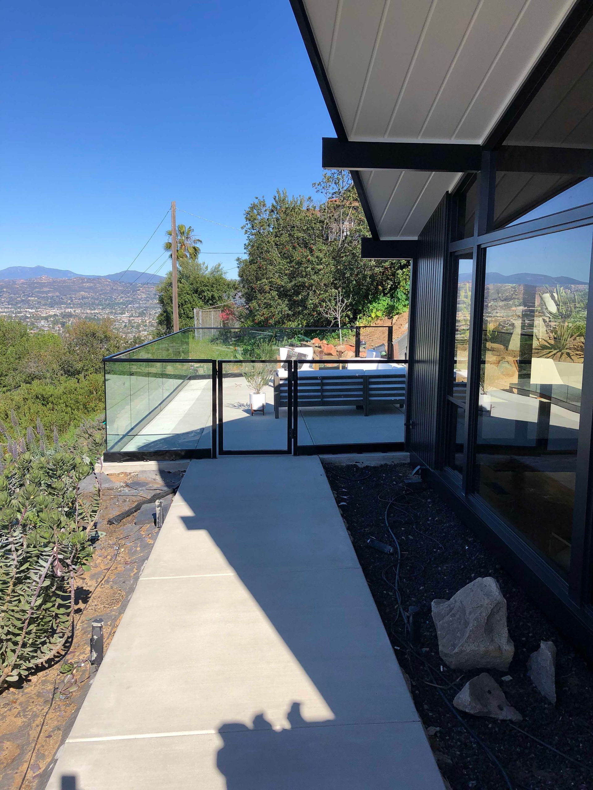 Exterior view of modern house with glass fence, walkway, and distant city view on a sunny day.