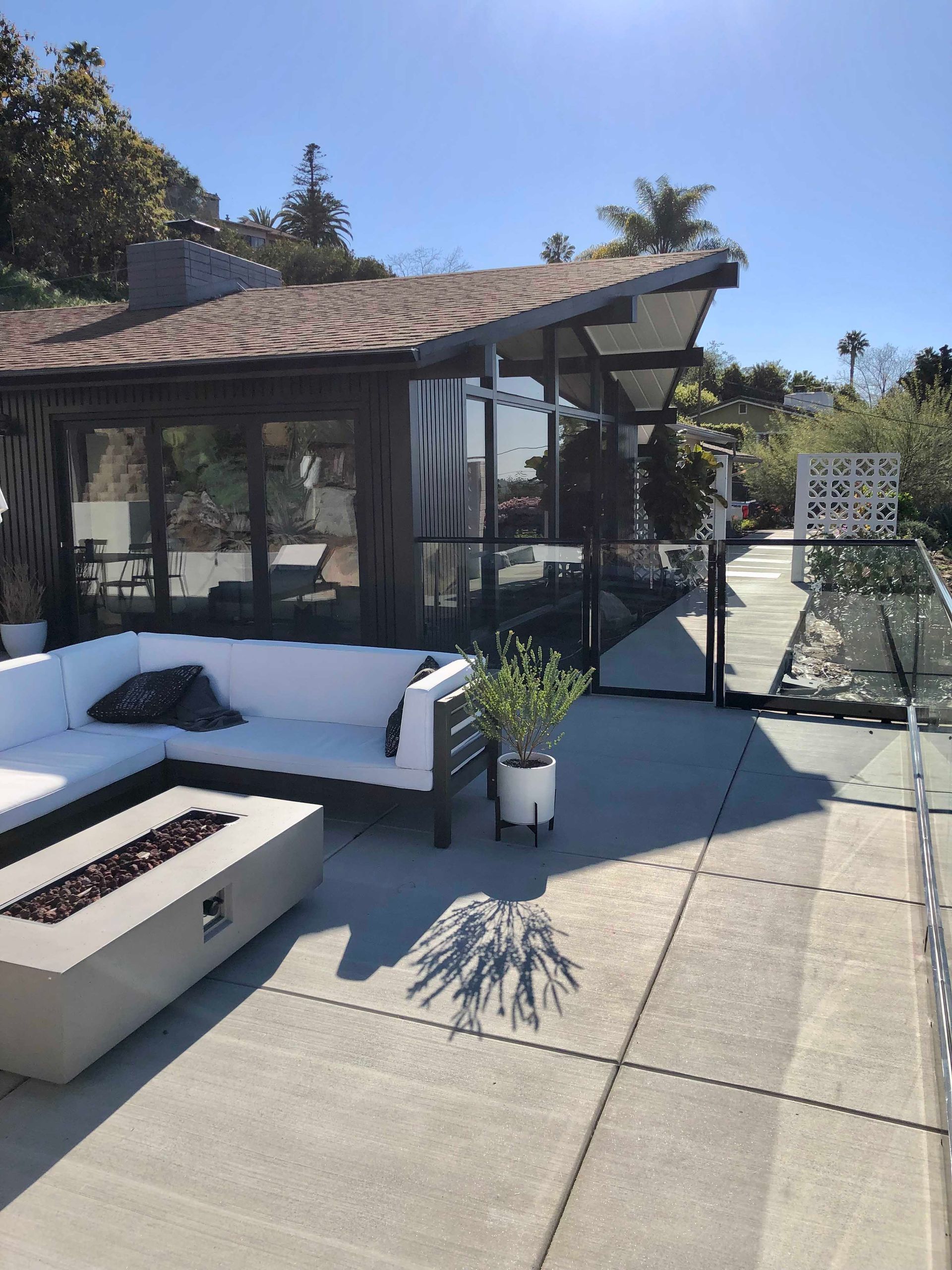 Outdoor patio with a white couch, fire pit, and enclosed seating area with glass walls and sloped roof.