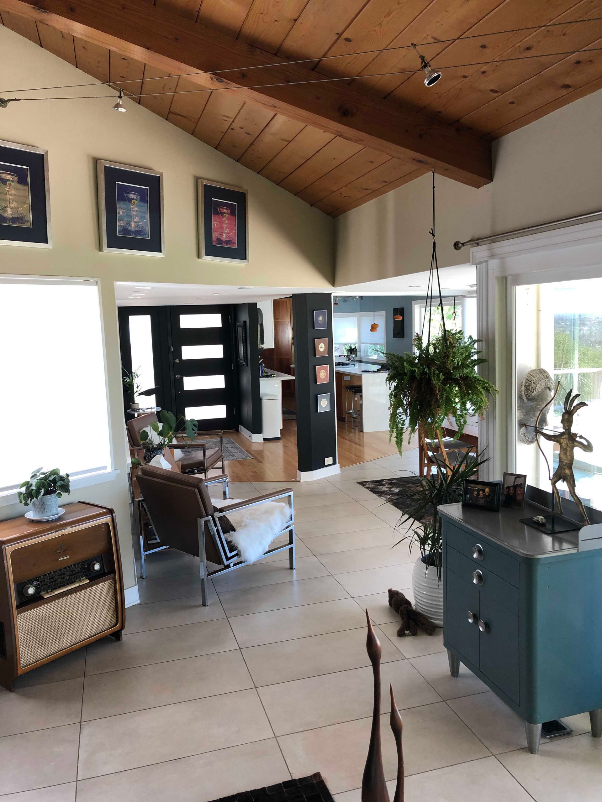 Bright living room with open floor plan, wood ceiling, framed jerseys, and a hanging plant.