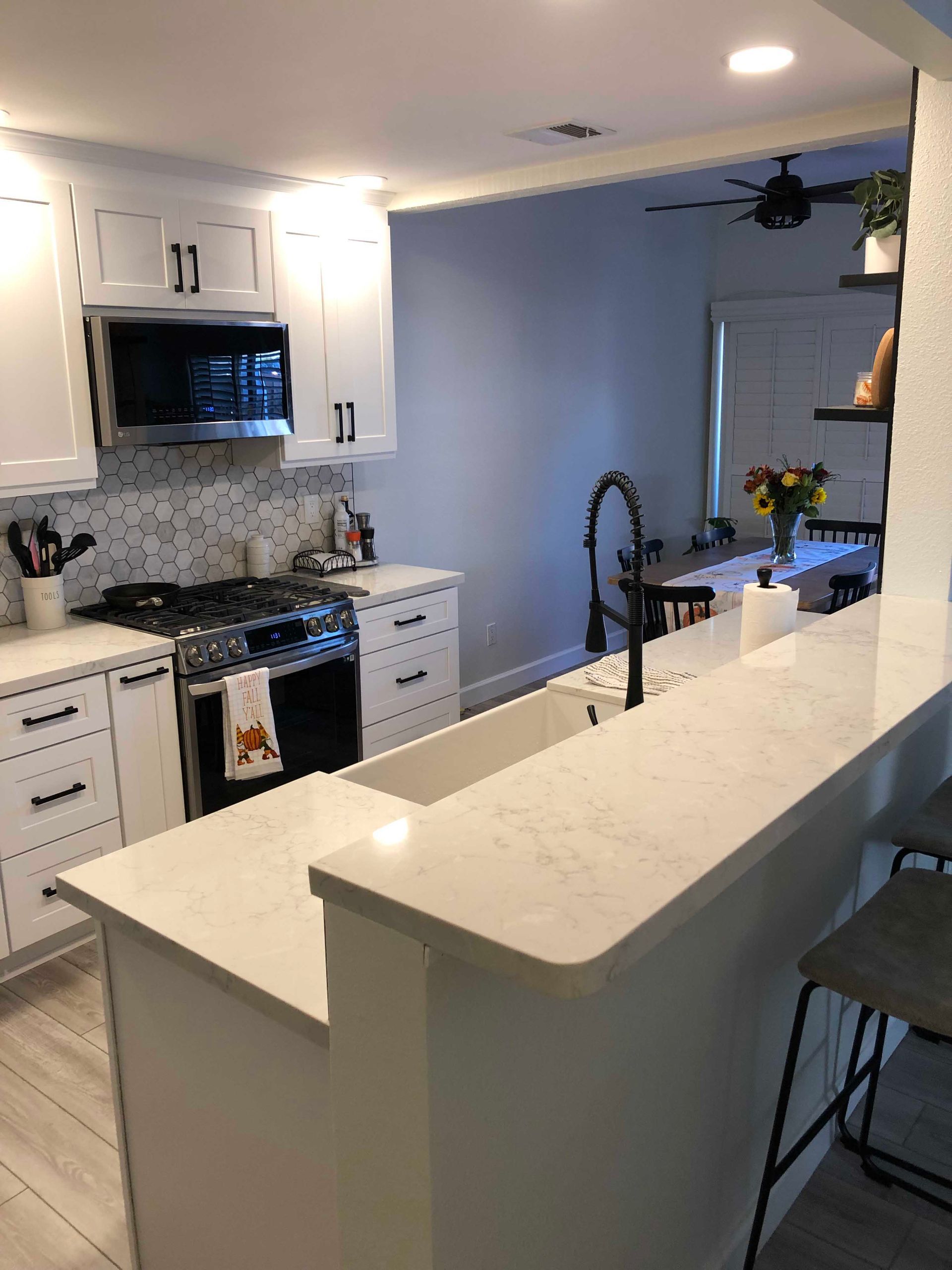 White kitchen with countertop, cabinets, and appliances. Black accents, leading to a dining area.