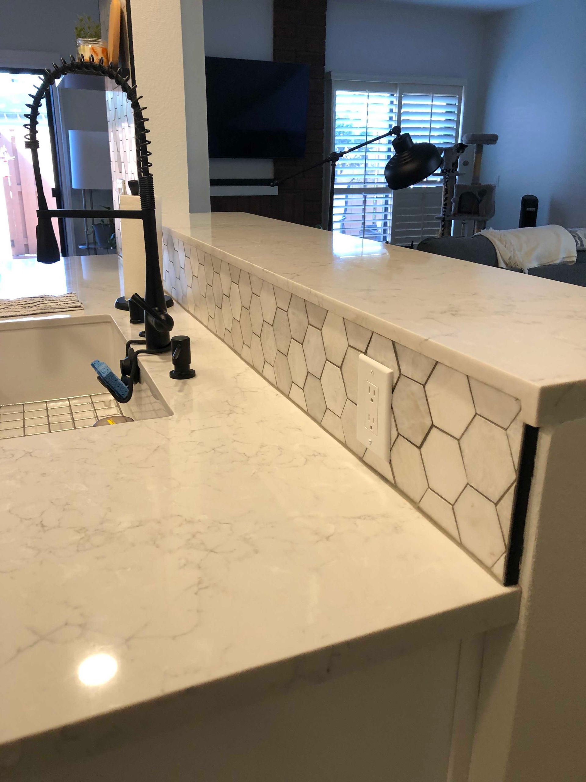 Kitchen counter with white quartz surface and hexagon tile backsplash, black faucet.