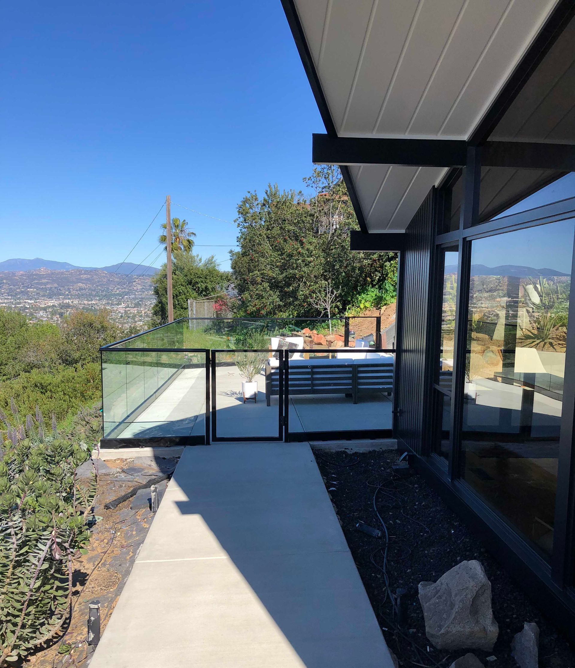 Modern house exterior with glass railing, concrete path, and scenic hillside view.