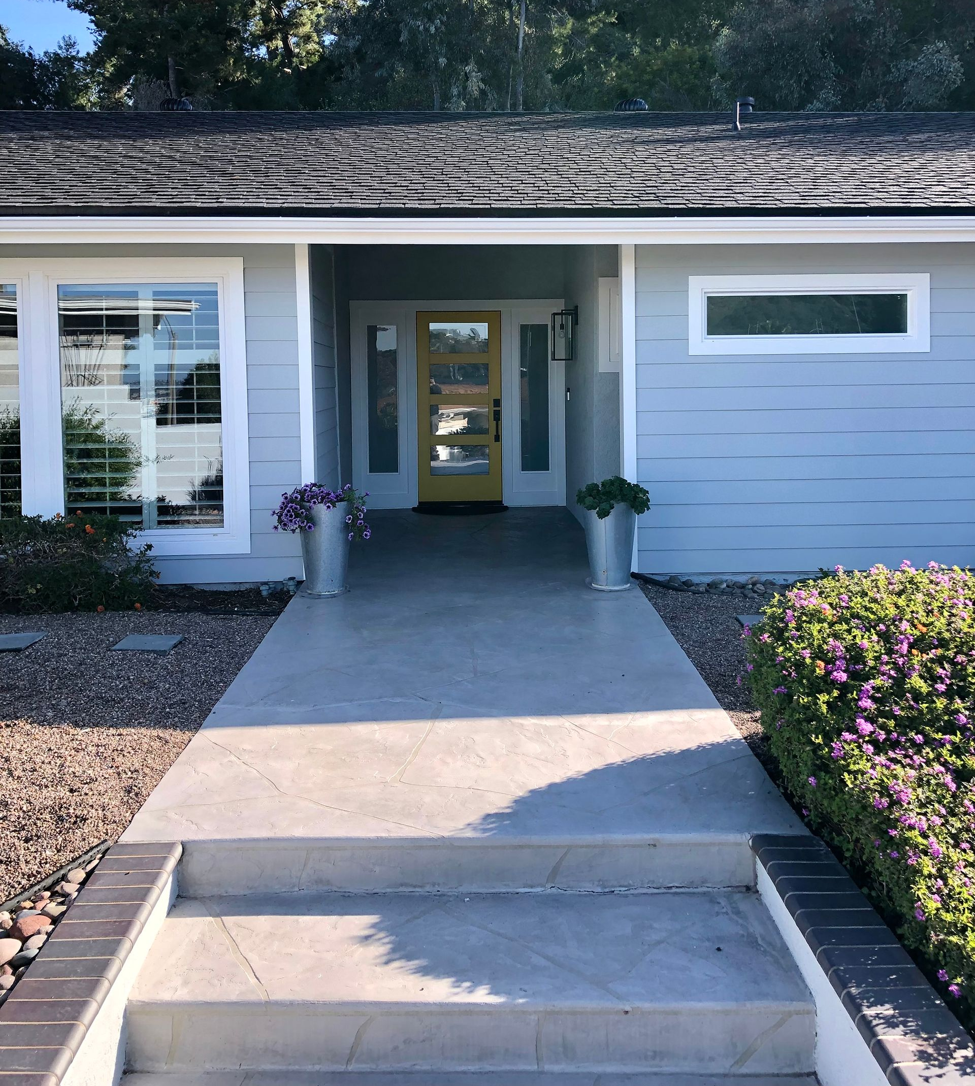 Light blue house with yellow front door, concrete path, and steps.