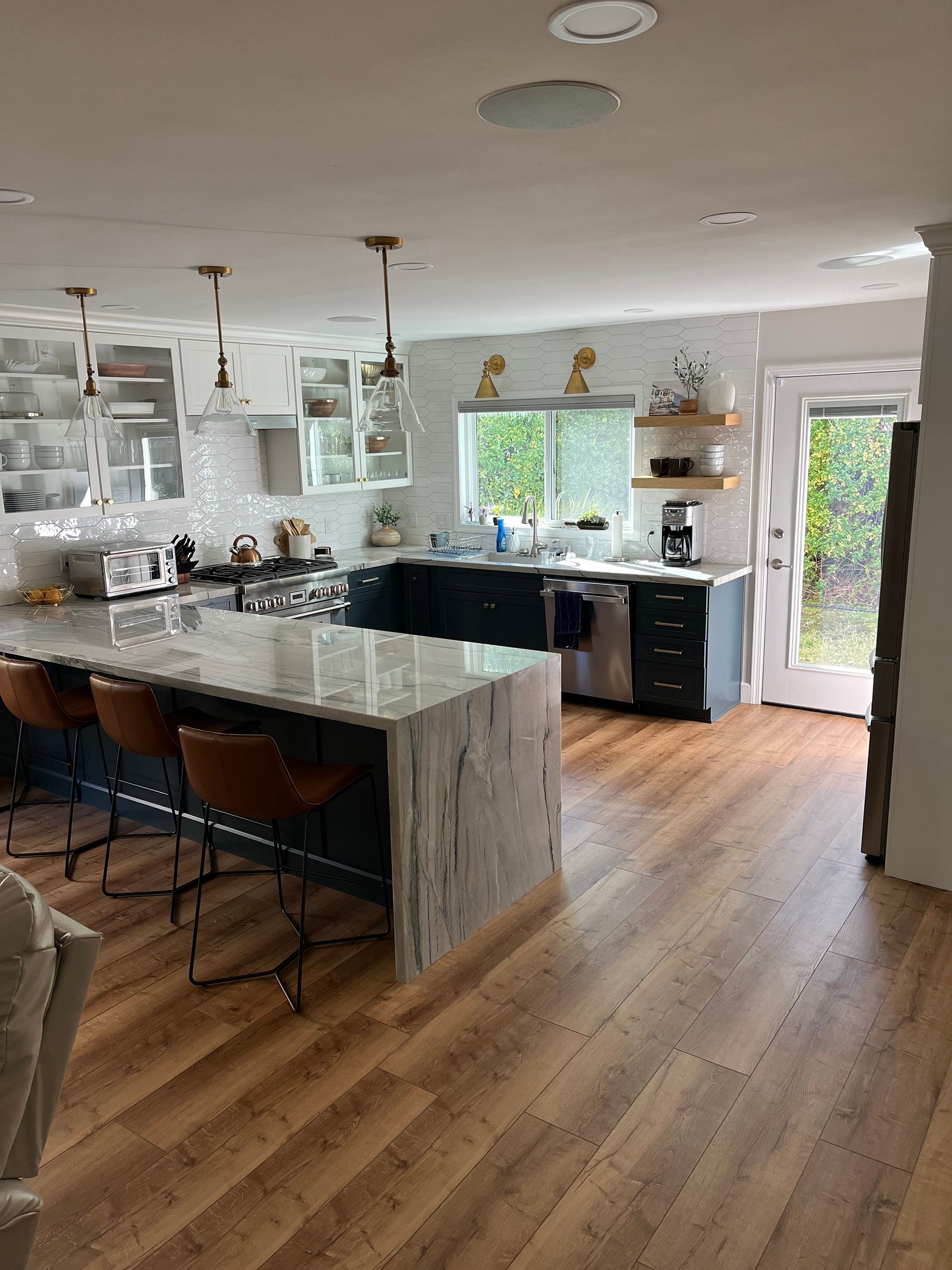 Modern kitchen with dark blue cabinets, marble island, and hardwood floors.