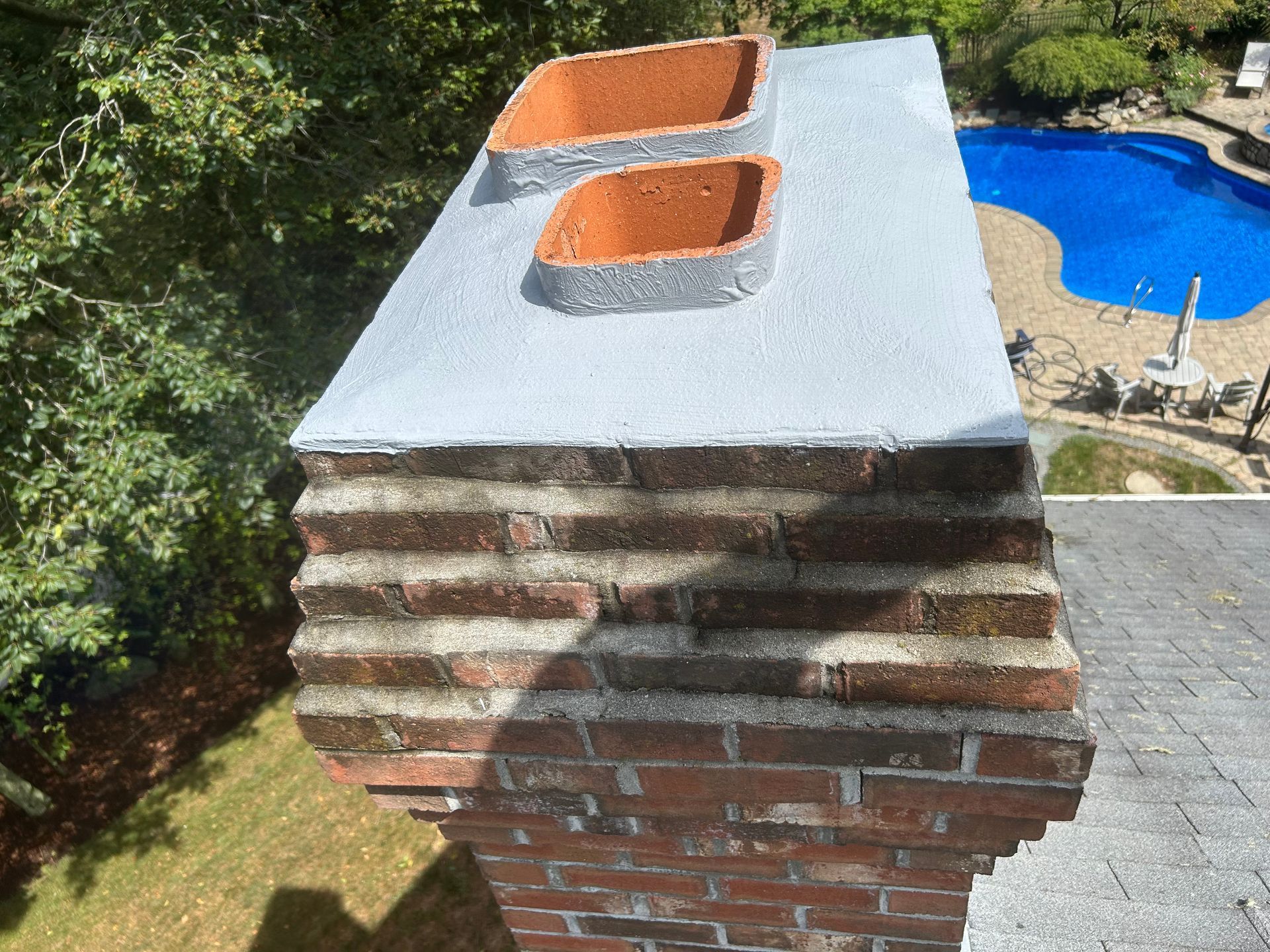 Brick chimney with white cap and two terracotta flue tiles beside a blue swimming pool