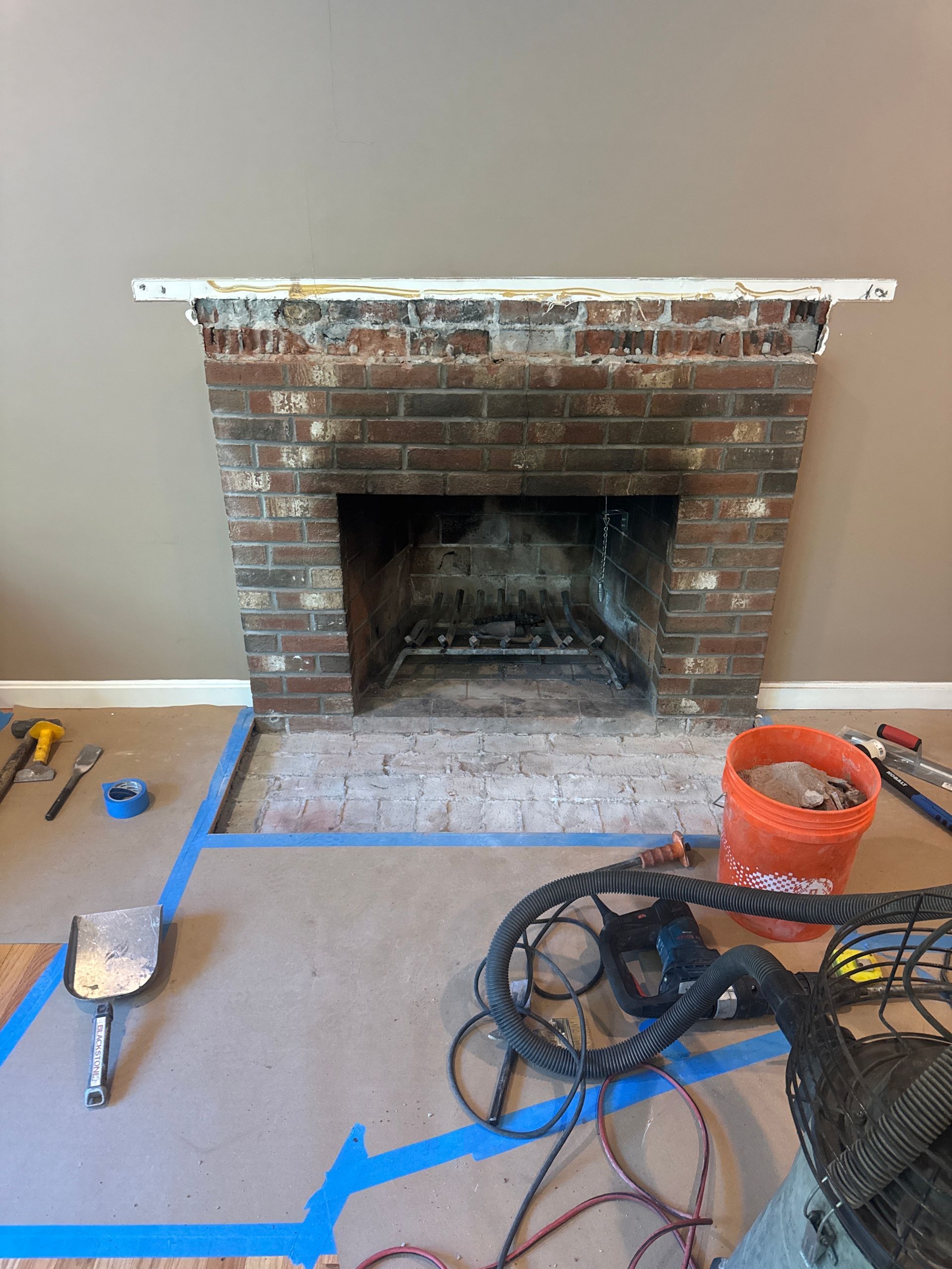 Brick fireplace under renovation with tools and cords on a work floor