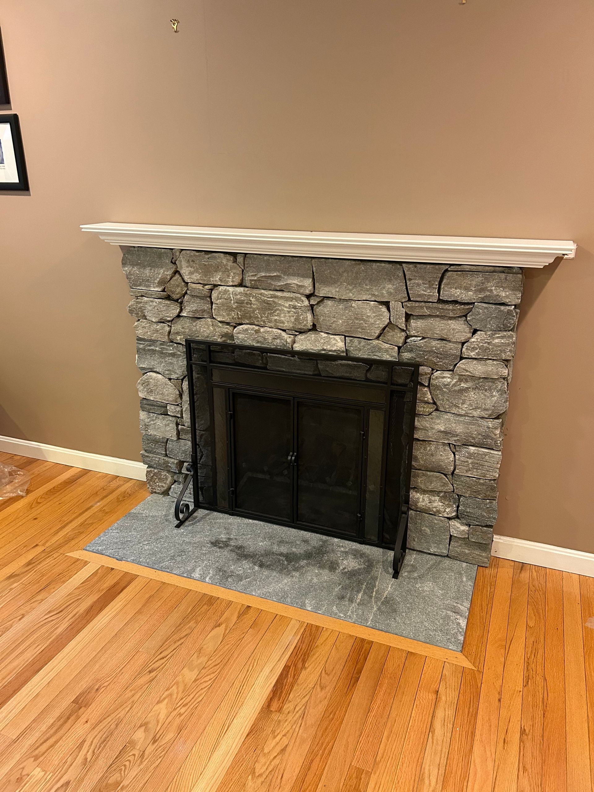 Stone fireplace with a white mantel in a room with hardwood floors and tan walls.