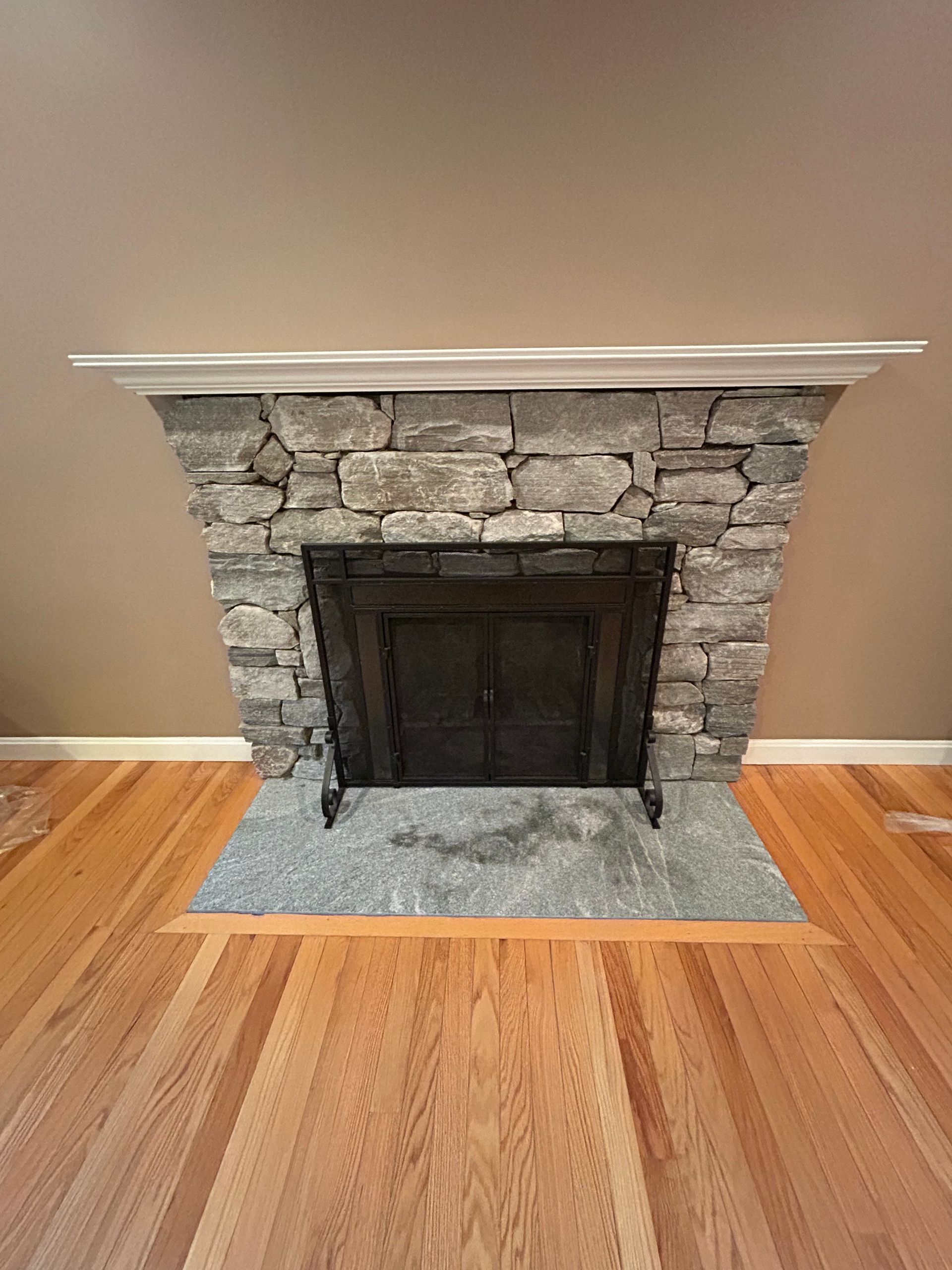 Stone fireplace with dark wood insert and white mantel on hardwood floor