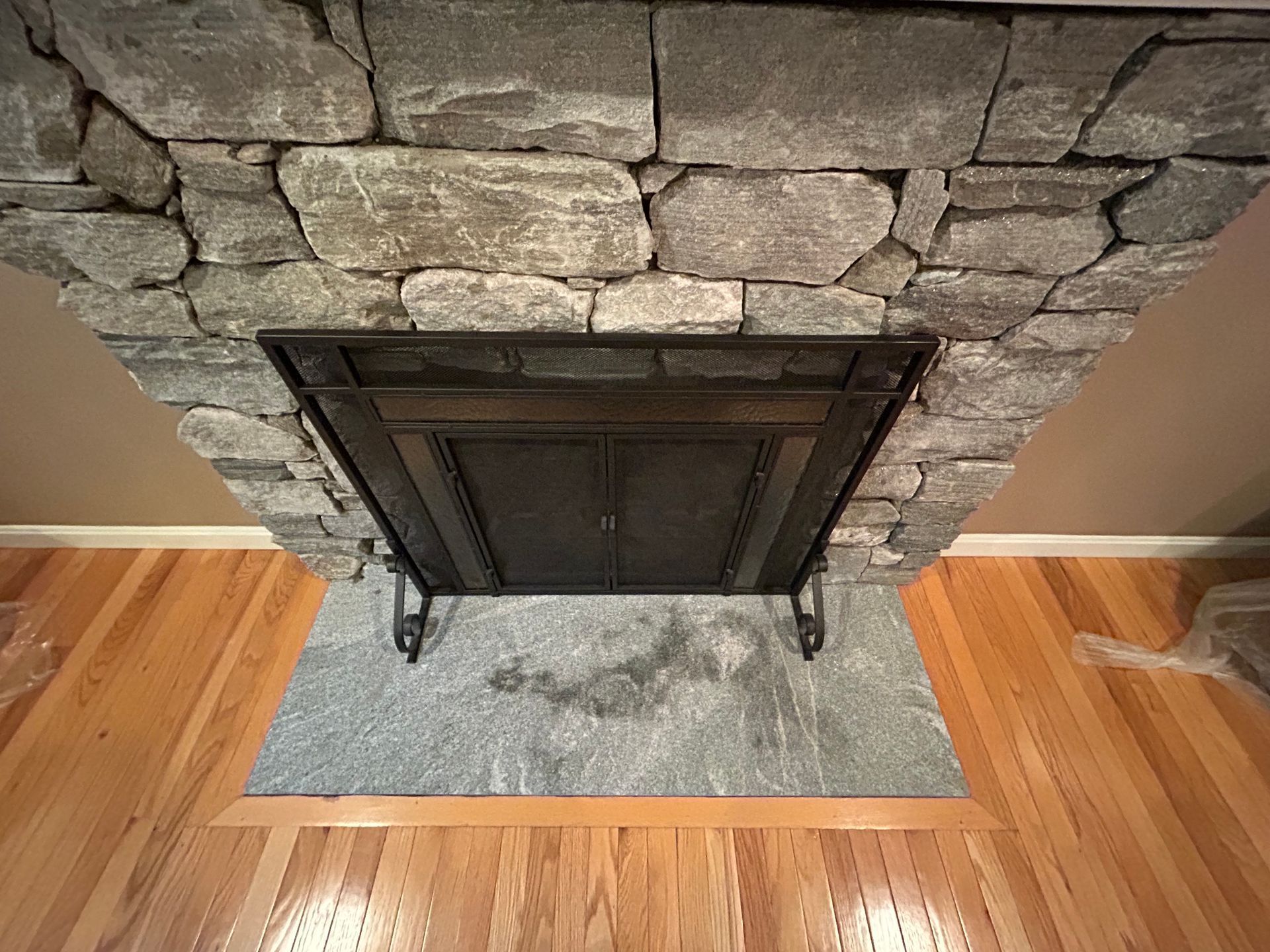 Stone fireplace with dark metal screen and wooden floor on either side