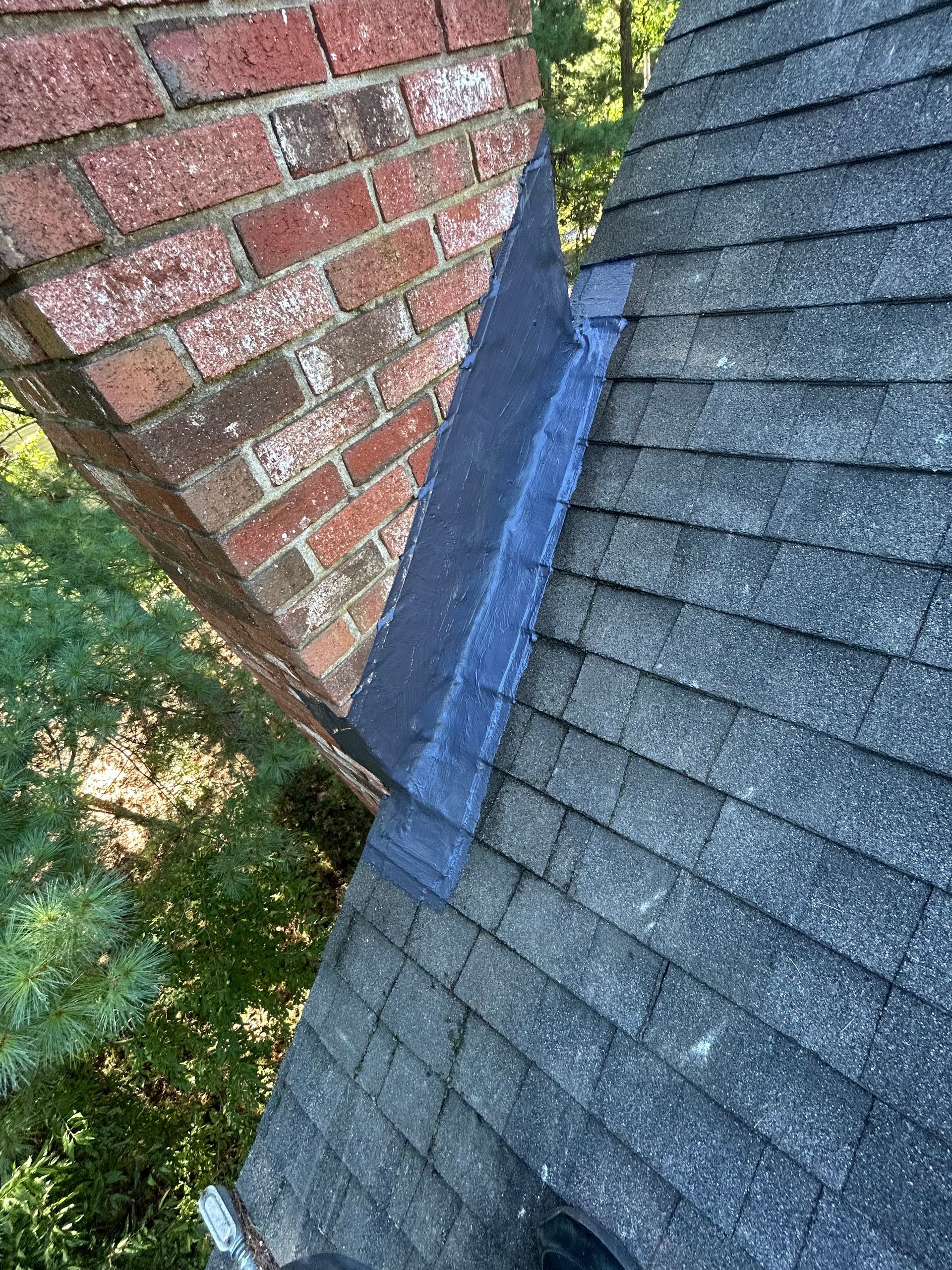 Roof shingles meeting a brick wall beside a blue flashing strip