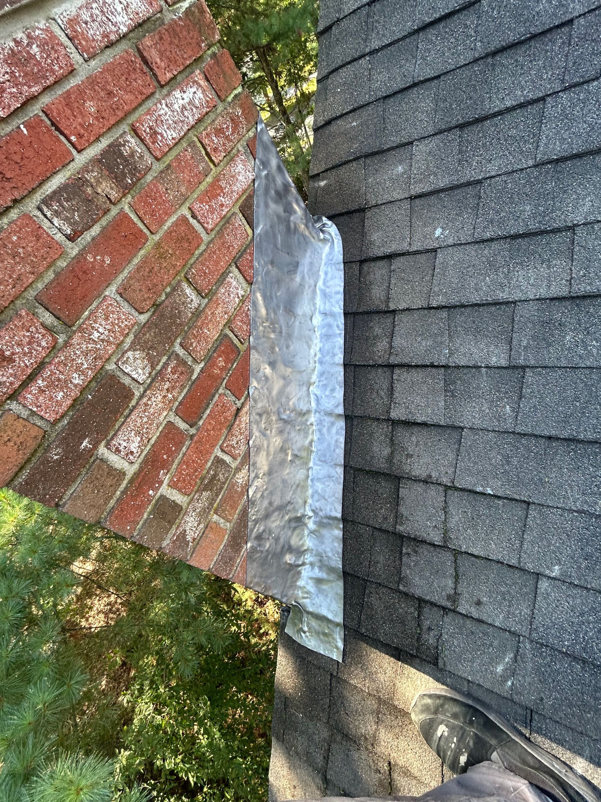 Damaged metal flashing between a red brick wall and gray shingle roof, with visible water staining