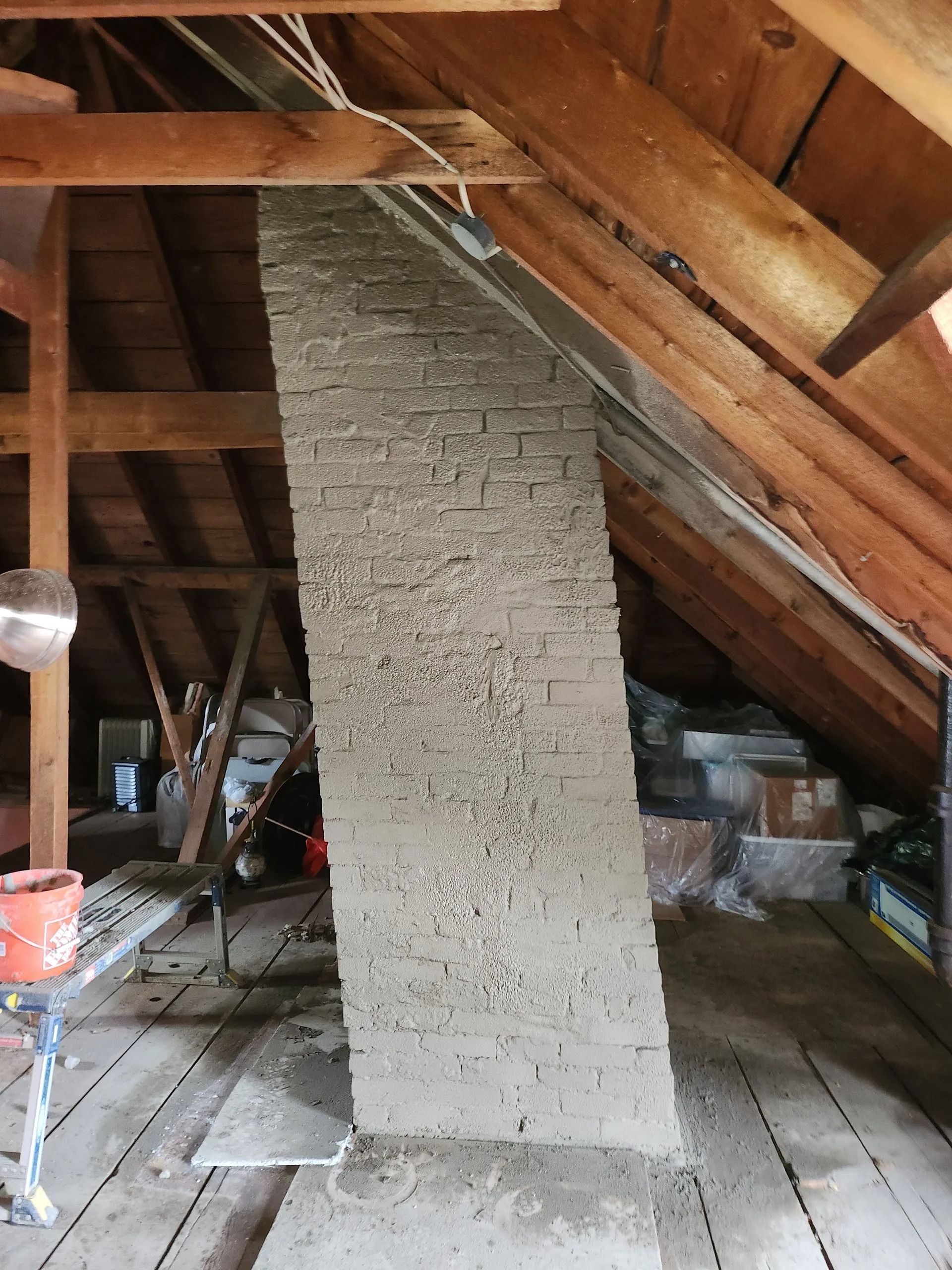 Brick chimney in attic, leaning against wooden beams and rafters. Natural light.
