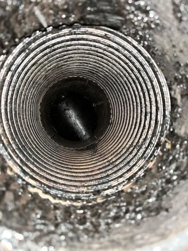 Looking down a metal, spiral-lined pipe.  Debris surrounds the opening.