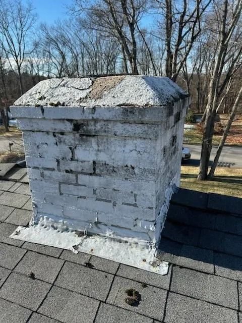 White-painted brick chimney on a roof, with worn and weathered appearance.
