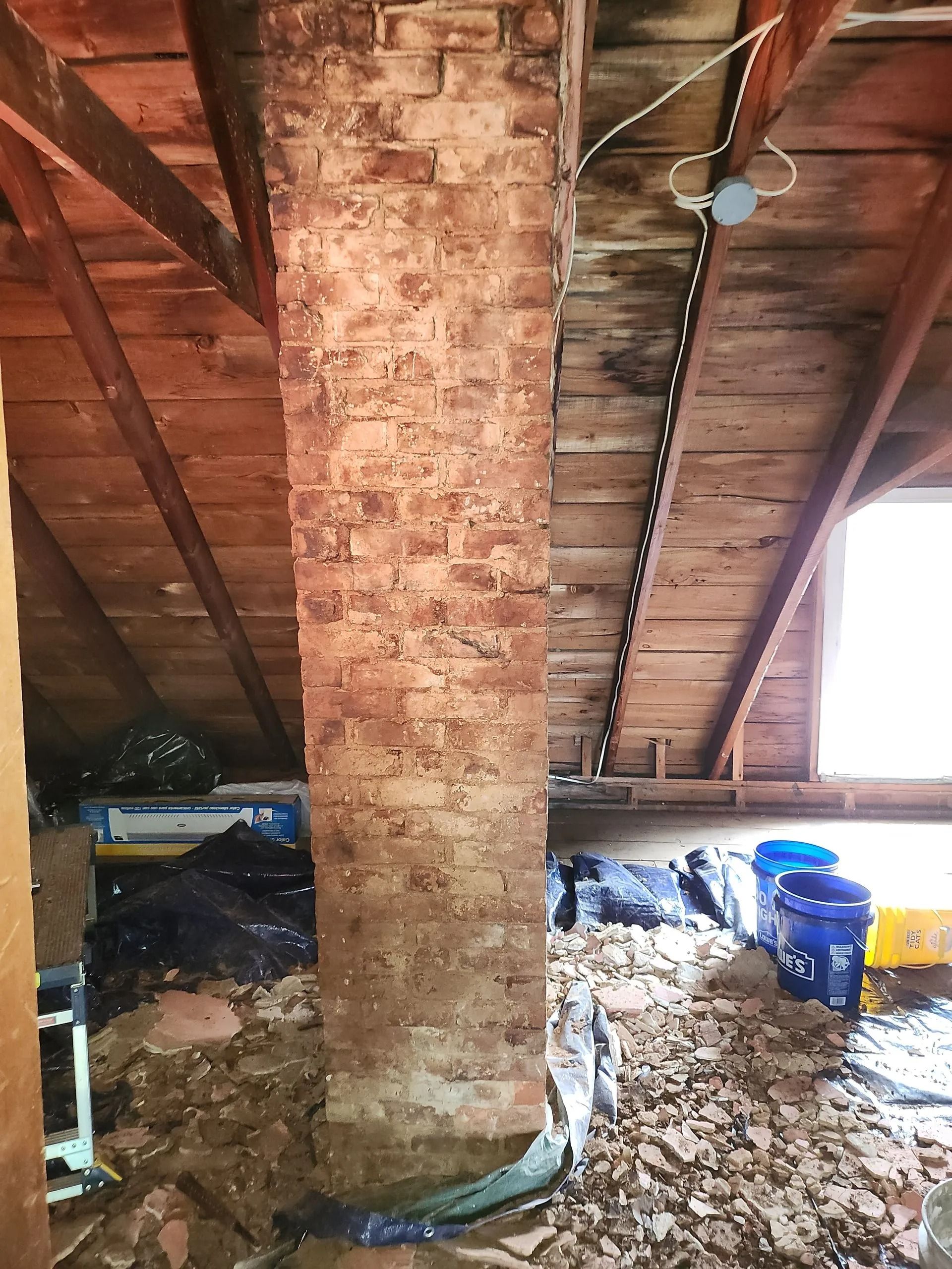 Brick chimney in an attic, with wooden rafters and insulation visible.