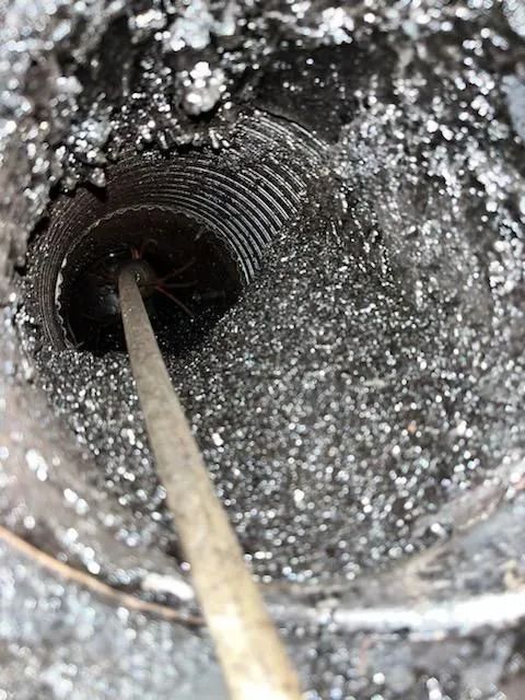 Inside view of a heavily sooted chimney. A cleaning rod is inside the flue.