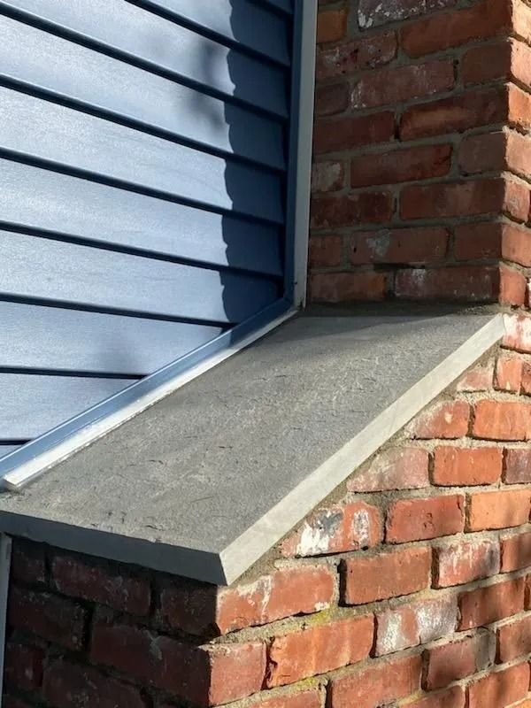 Blue siding, brick wall, and a gray concrete window sill.