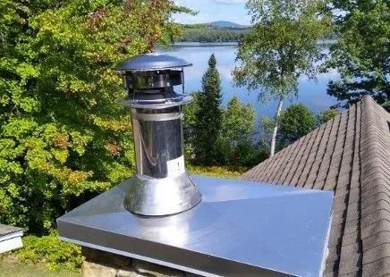 Stainless steel chimney on a house roof, lake and trees in the background.