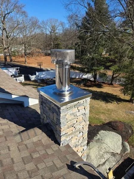 Chimney with stainless steel cap and stone facade on a roof, sunny day.