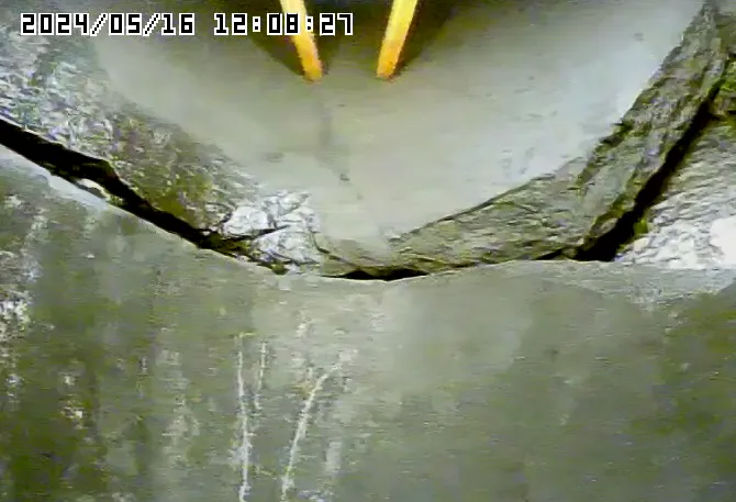 Close-up of a cracked concrete surface. A deep crack divides the concrete, with a timestamp in the top left corner.