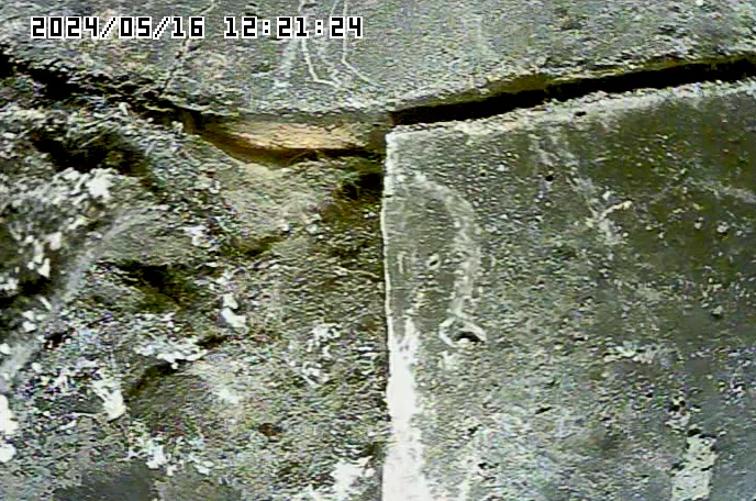 Close-up of a damaged, cracked concrete surface. Visible are dark gray and light yellow areas, with the date and time in top left corner.
